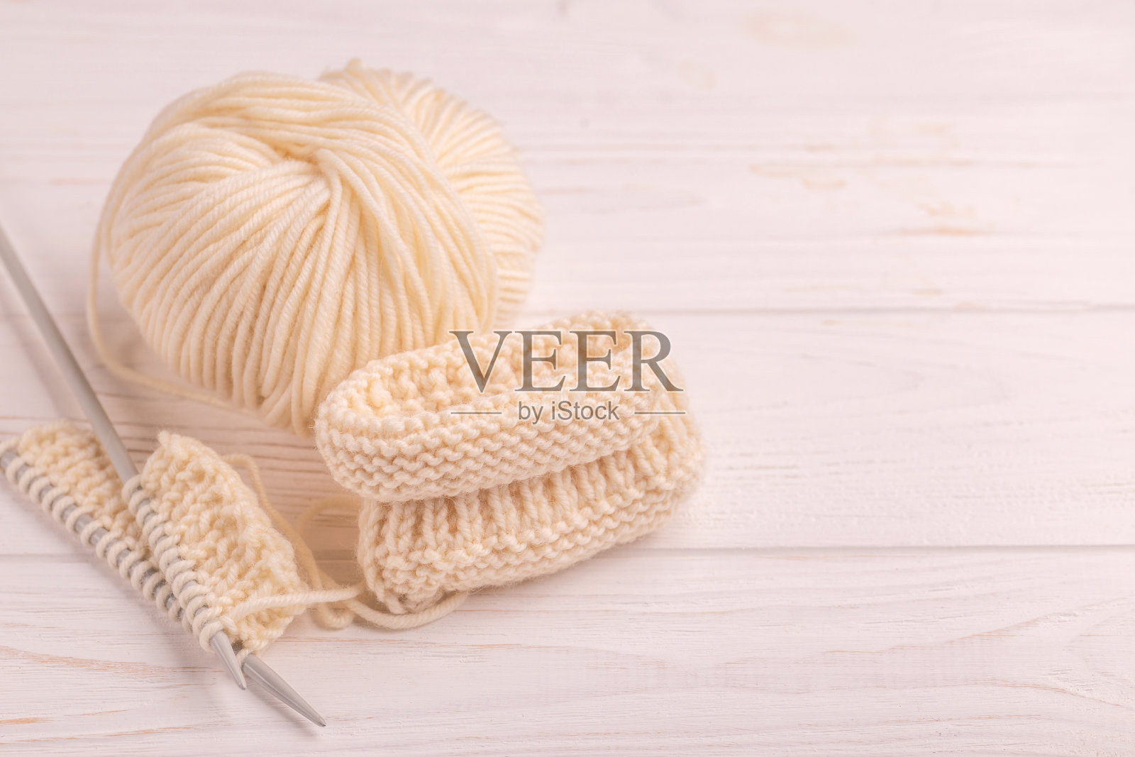 用纱线和针在白色木制背景上编织婴儿短靴。照片摄影图片