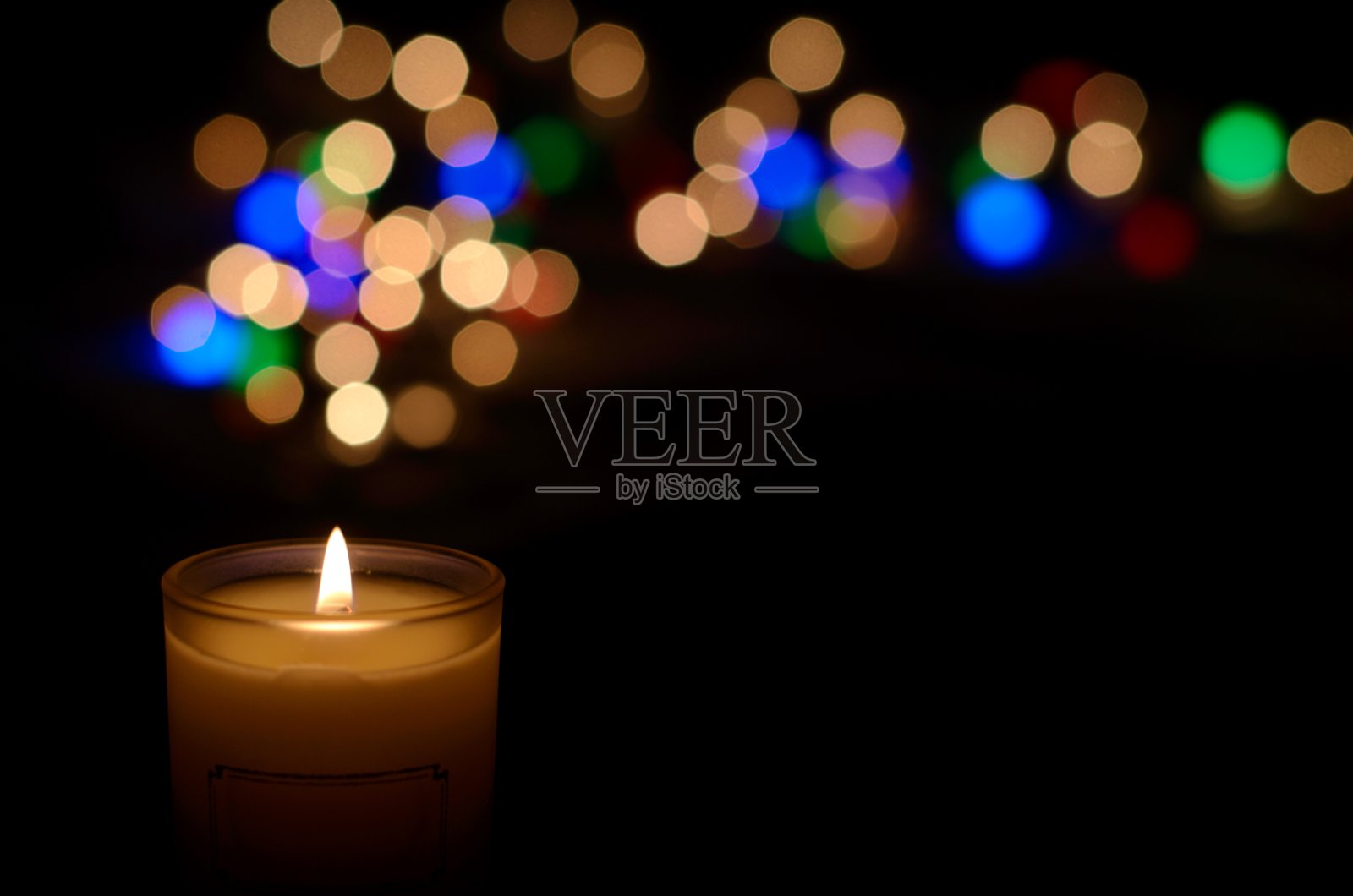 白色芳香玻璃蜡烛火焰和彩色圆形散焦在黑暗的背景为圣诞假期。照片摄影图片