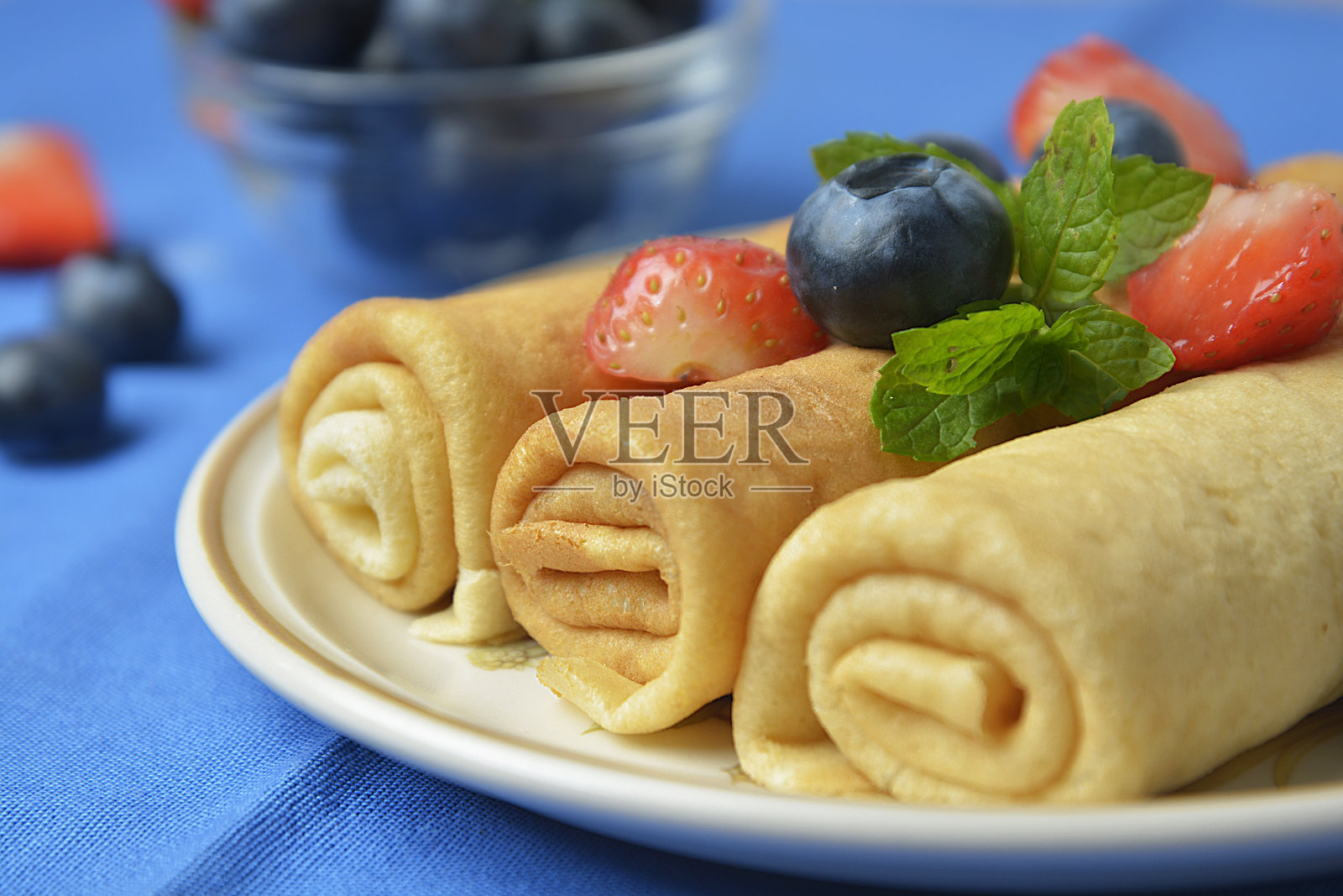 卷起来的可丽饼、薄煎饼和蓝莓、草莓放在盘子里。垂直的图像。照片摄影图片