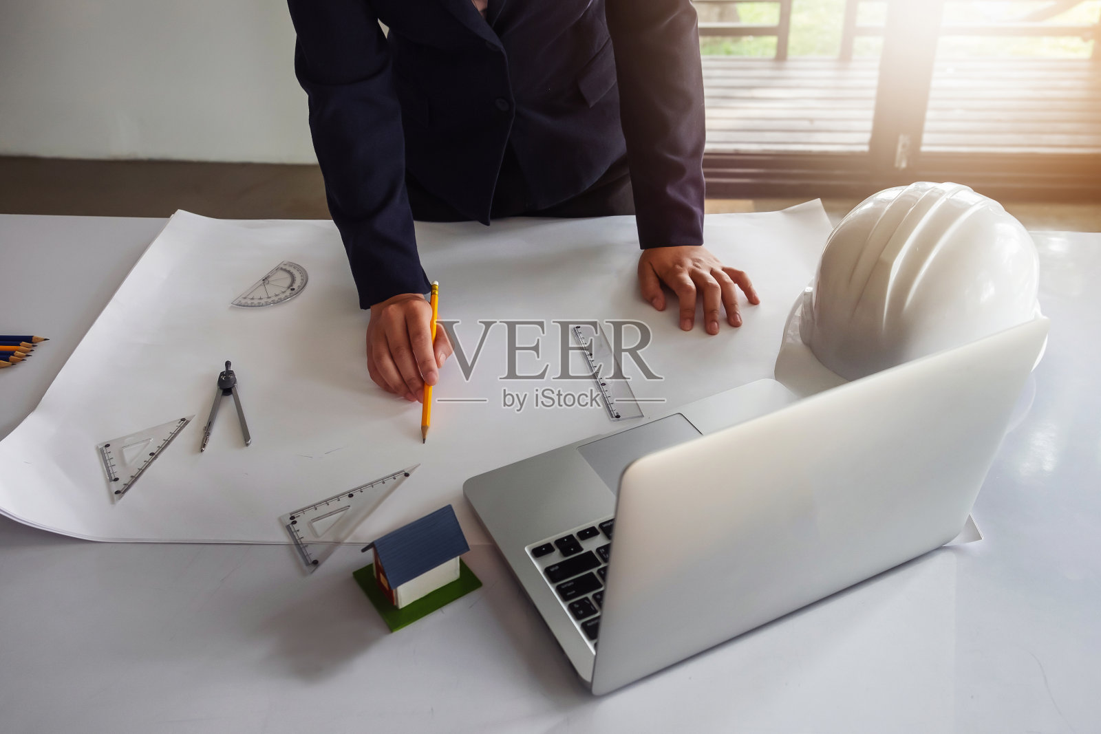 年轻的工程师们拿着一支黄色的笔指着设计图上的一座建筑，正在用笔记本电脑为工作现场的会议写报告。照片摄影图片