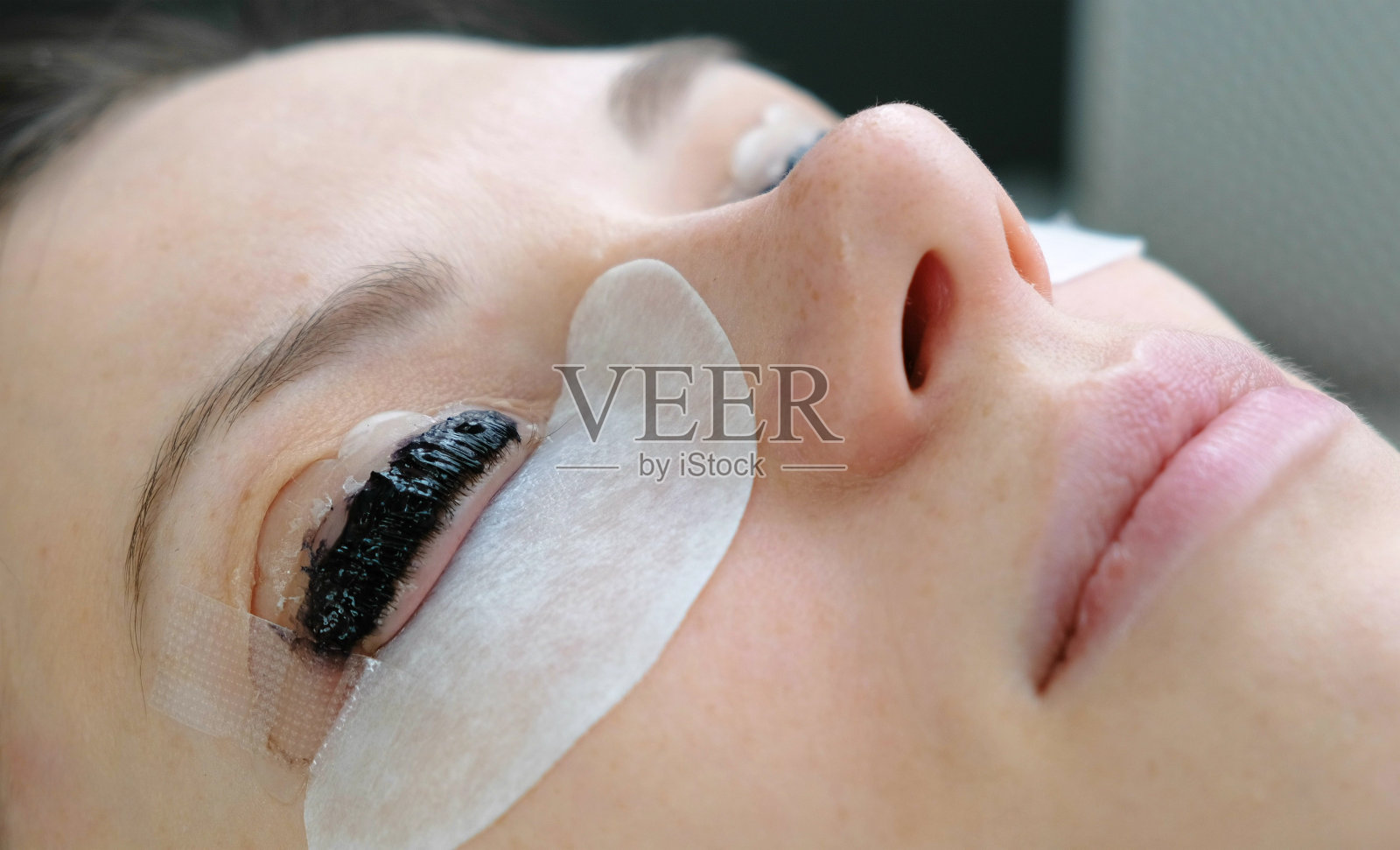 美容治疗。特写女人的脸，涂上睫毛。贴合睫毛。侧视图。照片摄影图片