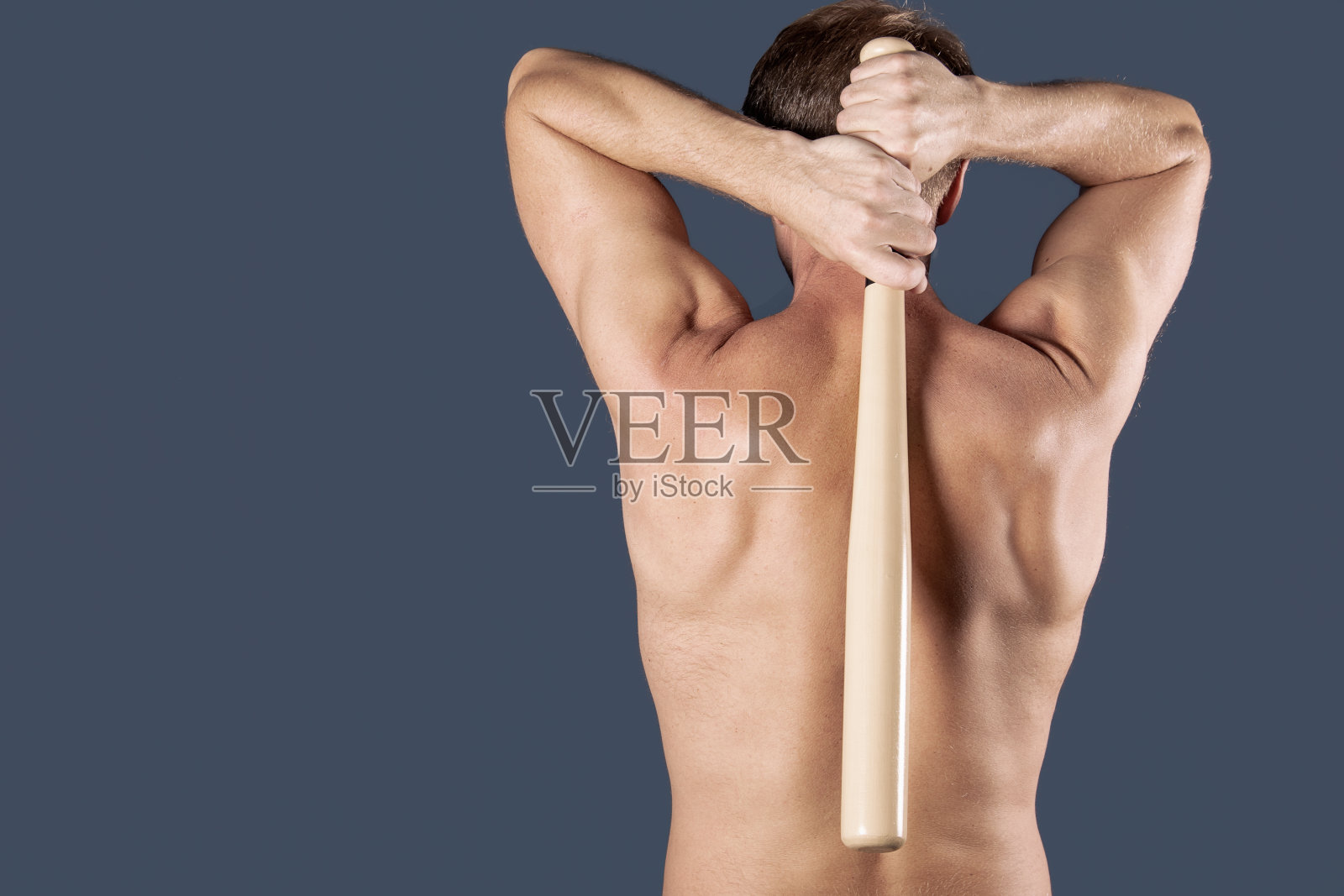 赤膊男子在他的背后拿着一个棒球棒在蓝色的背景照片摄影图片