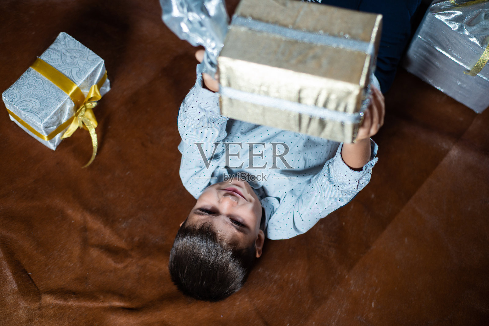 抱着礼品盒坐在地板上的小男孩，圣诞快乐照片摄影图片