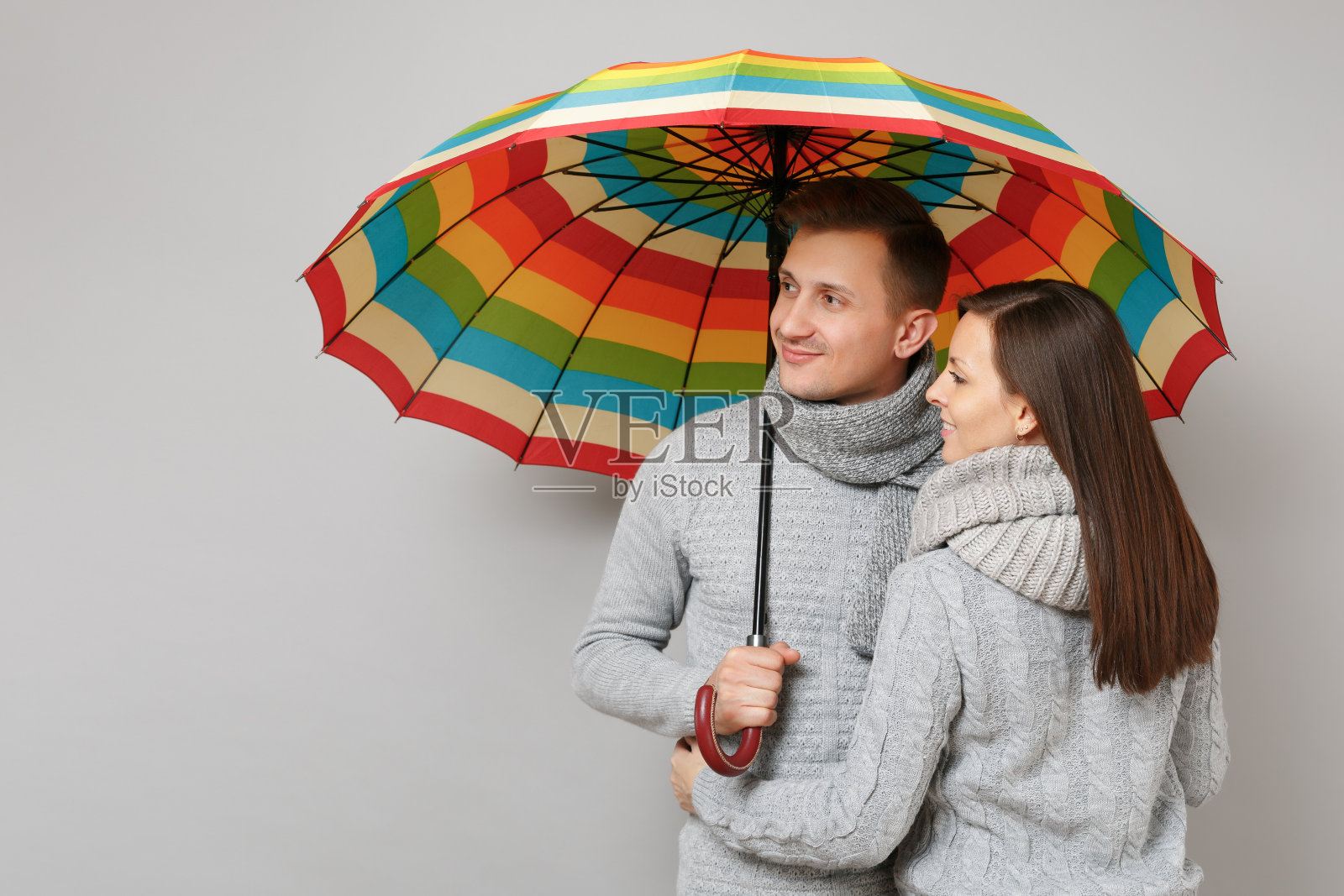 一对女孩男生穿着灰色毛衣围着围巾一起撑伞，孤立在灰色墙壁的背景下，照相馆肖像。健康的生活方式生病生病疾病治疗寒冷季节的概念。模拟拷贝空间照片摄影图片