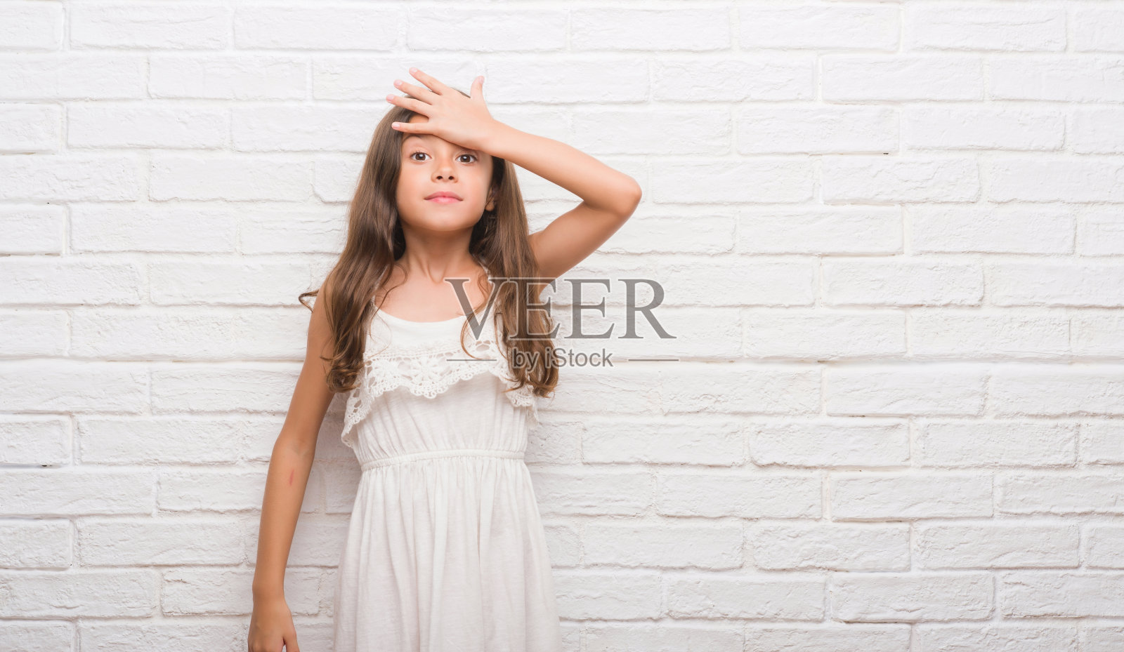 年轻的西班牙孩子越过白砖墙惊讶地用手顶着错误，记得错误。忘记，糟糕的记忆概念。照片摄影图片