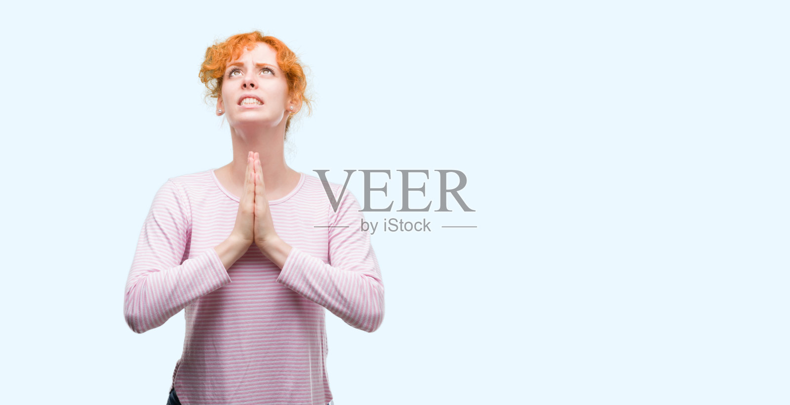 年轻的红发女子手拉着手乞求和祈祷，脸上带着希望的表情，非常激动和担心。请求宽恕。宗教的概念。照片摄影图片