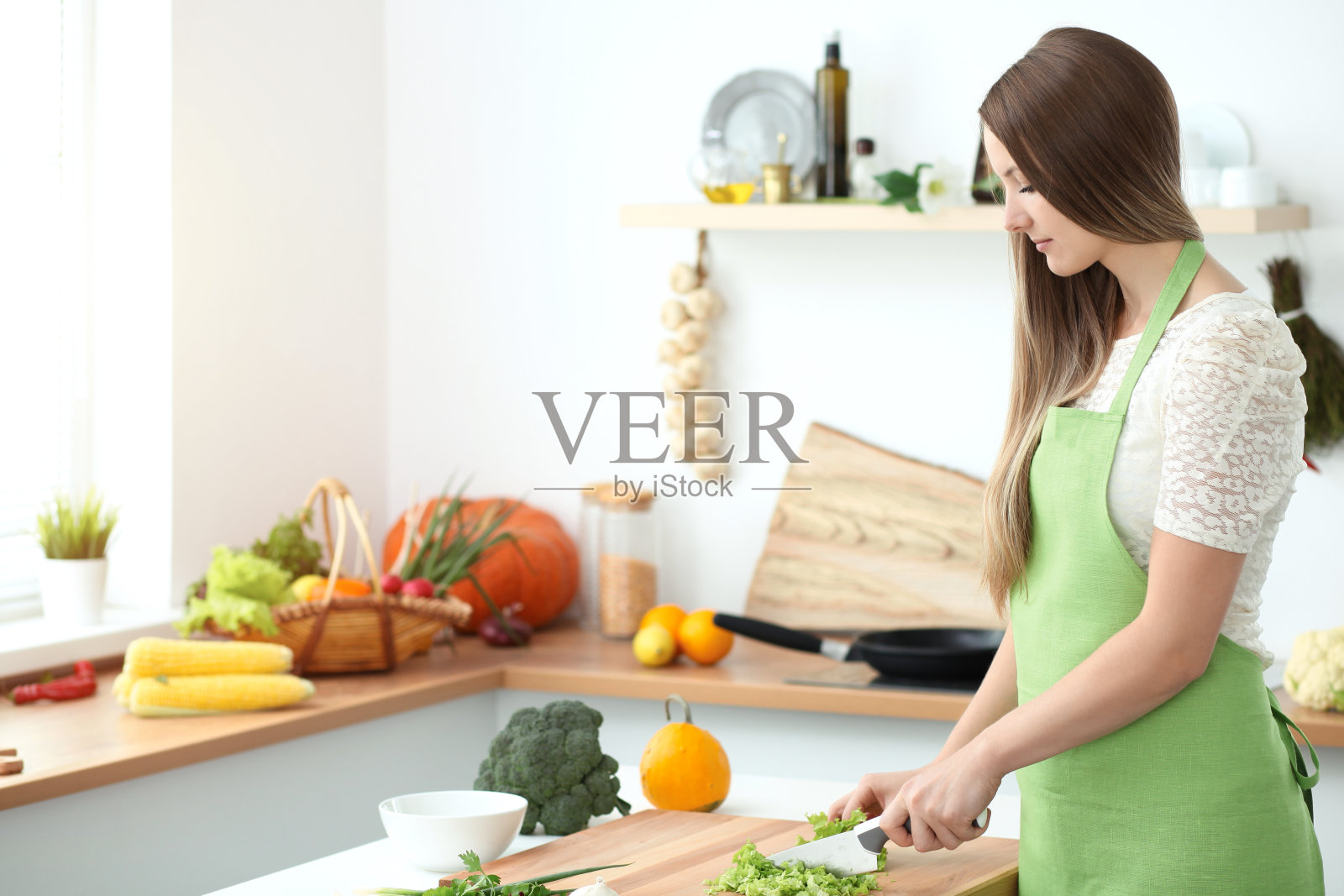 年轻女子在厨房做饭。主妇切片ââ新鲜沙拉。照片摄影图片