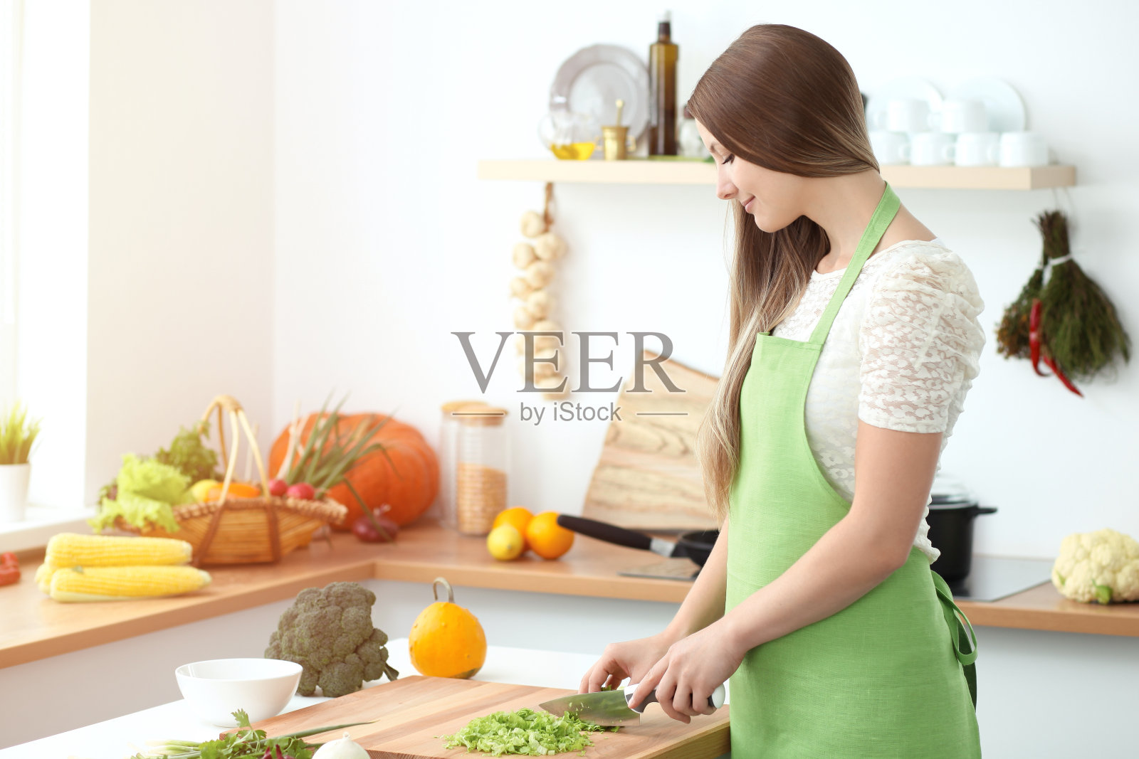 年轻女子在厨房做饭。主妇切片ââ新鲜沙拉。照片摄影图片