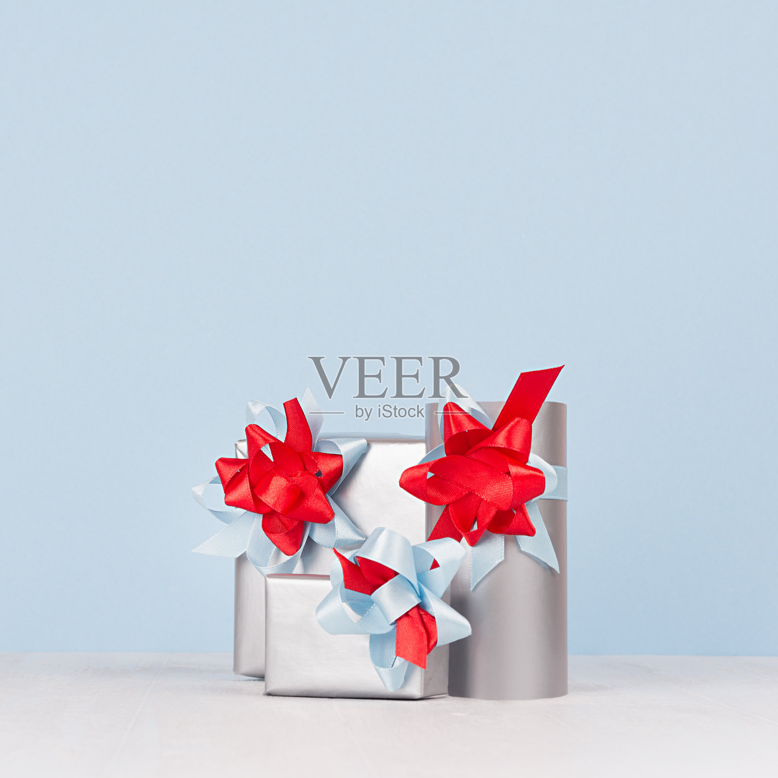 明亮的金属纸礼品盒与红色和蓝色缎带和蝴蝶结在柔软的轻白色木板。照片摄影图片