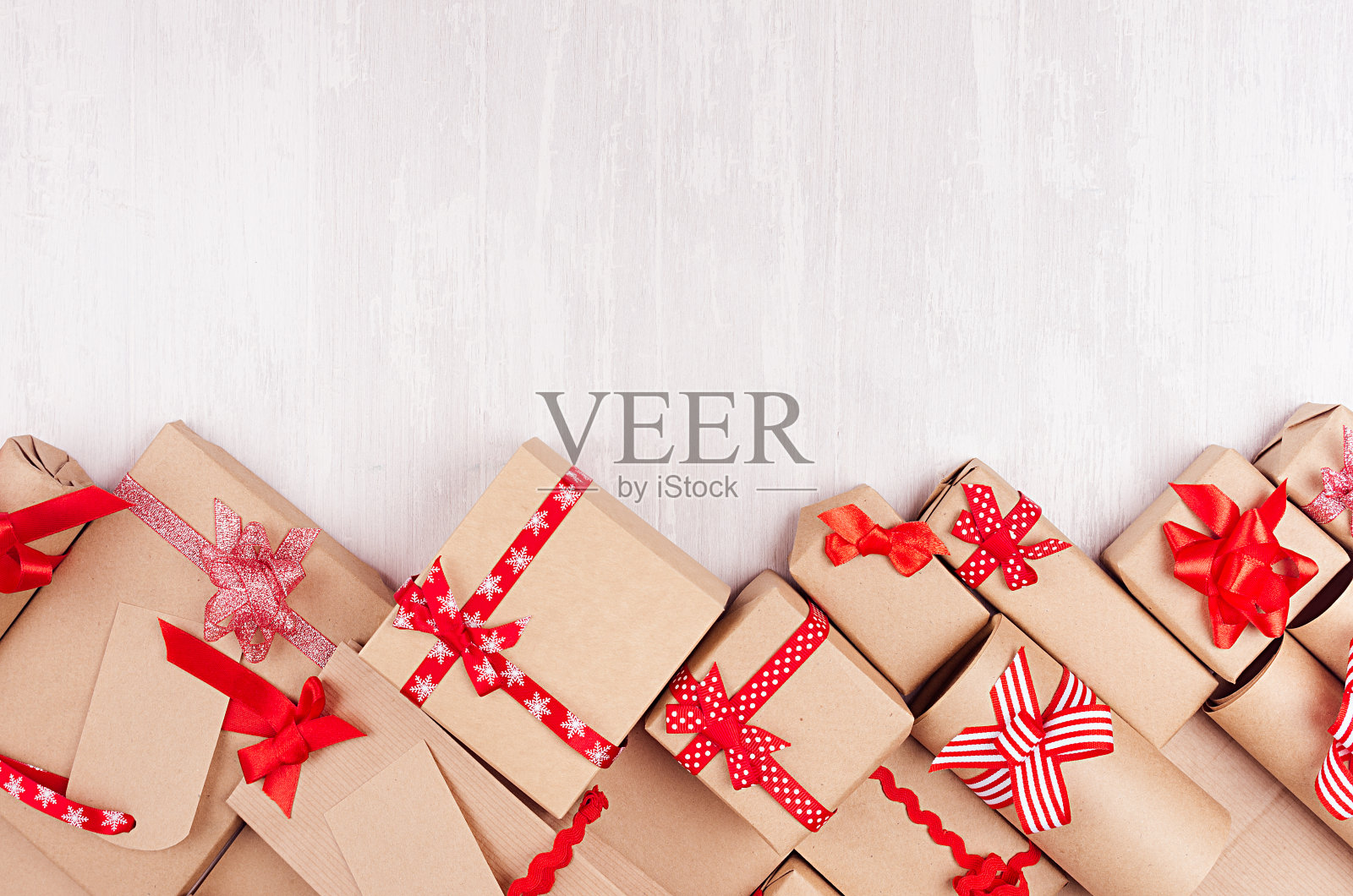 庆祝礼品背景-用红丝带和蝴蝶结包装的不同的牛皮纸礼物，白色木桌上的空白标签，复制空间。照片摄影图片