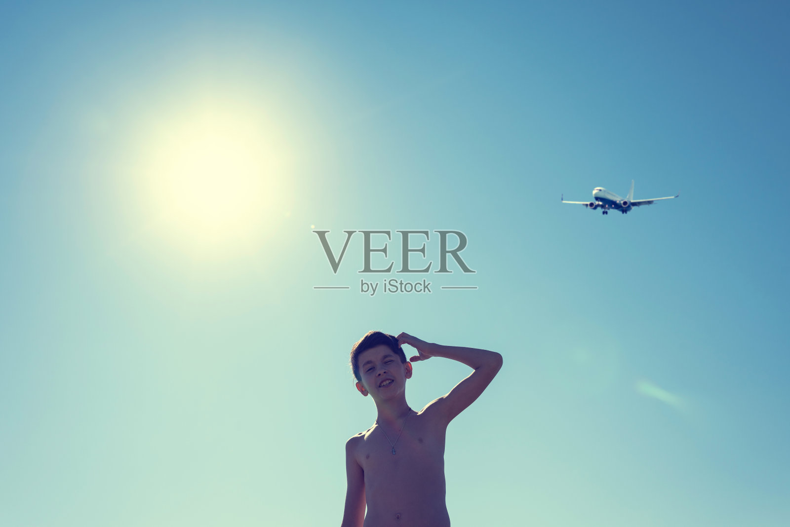 十几岁男孩的剪影在海滩上戴着耳机对面的阳光降落飞机。和孩子们一起乘飞机旅行。照片摄影图片