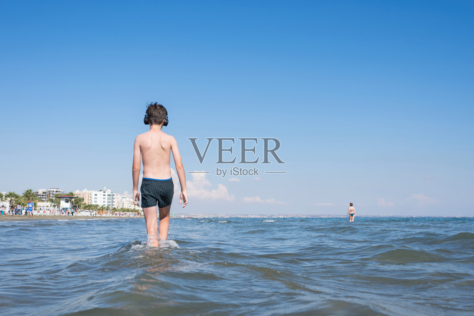 十几岁的男孩在海浪的海滩上戴着耳机。照片摄影图片