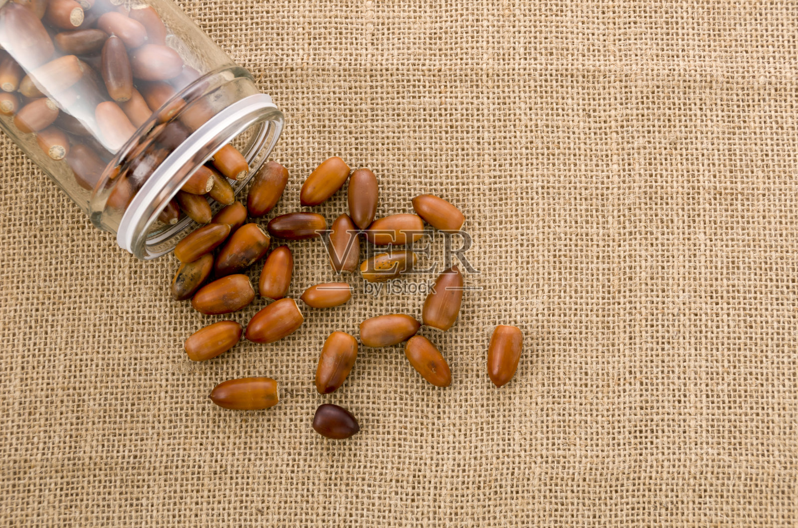 玻璃罐与橡子在粗麻布的背景照片摄影图片