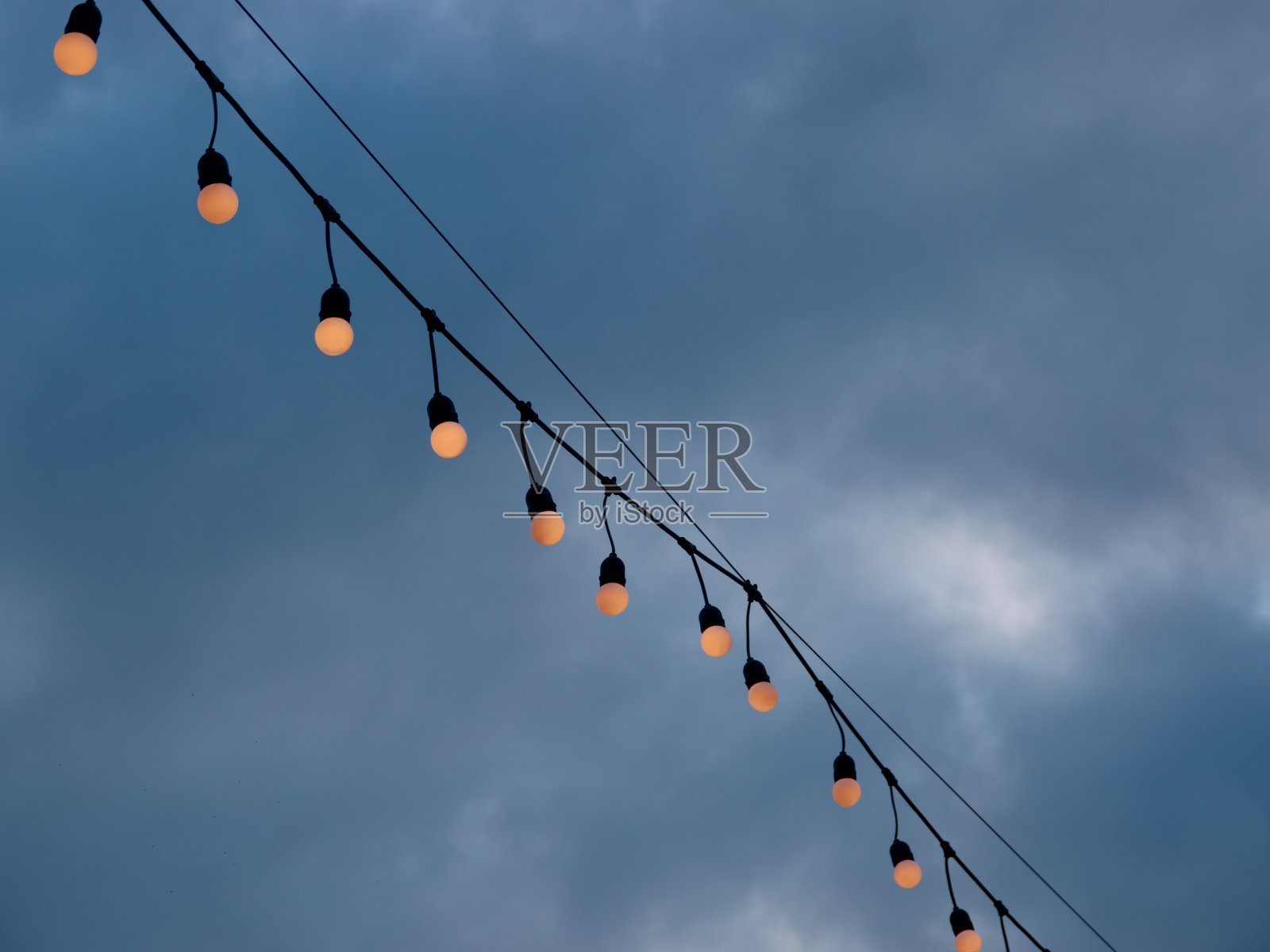 在多云的天空背景下，灯泡挂在电线上照片摄影图片