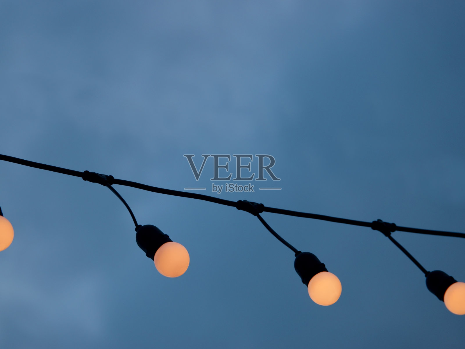 在多云的天空背景下，灯泡挂在电线上照片摄影图片