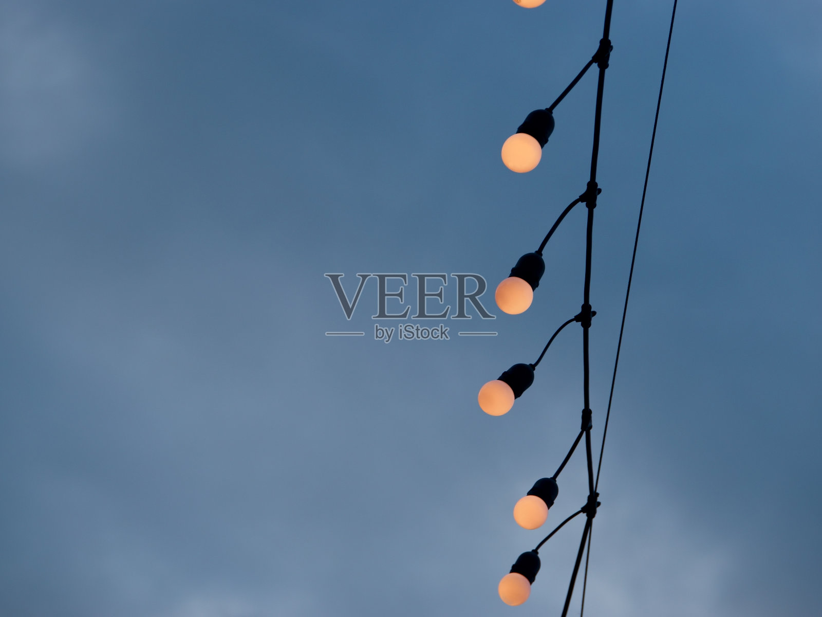 在多云的天空背景下，灯泡挂在电线上照片摄影图片