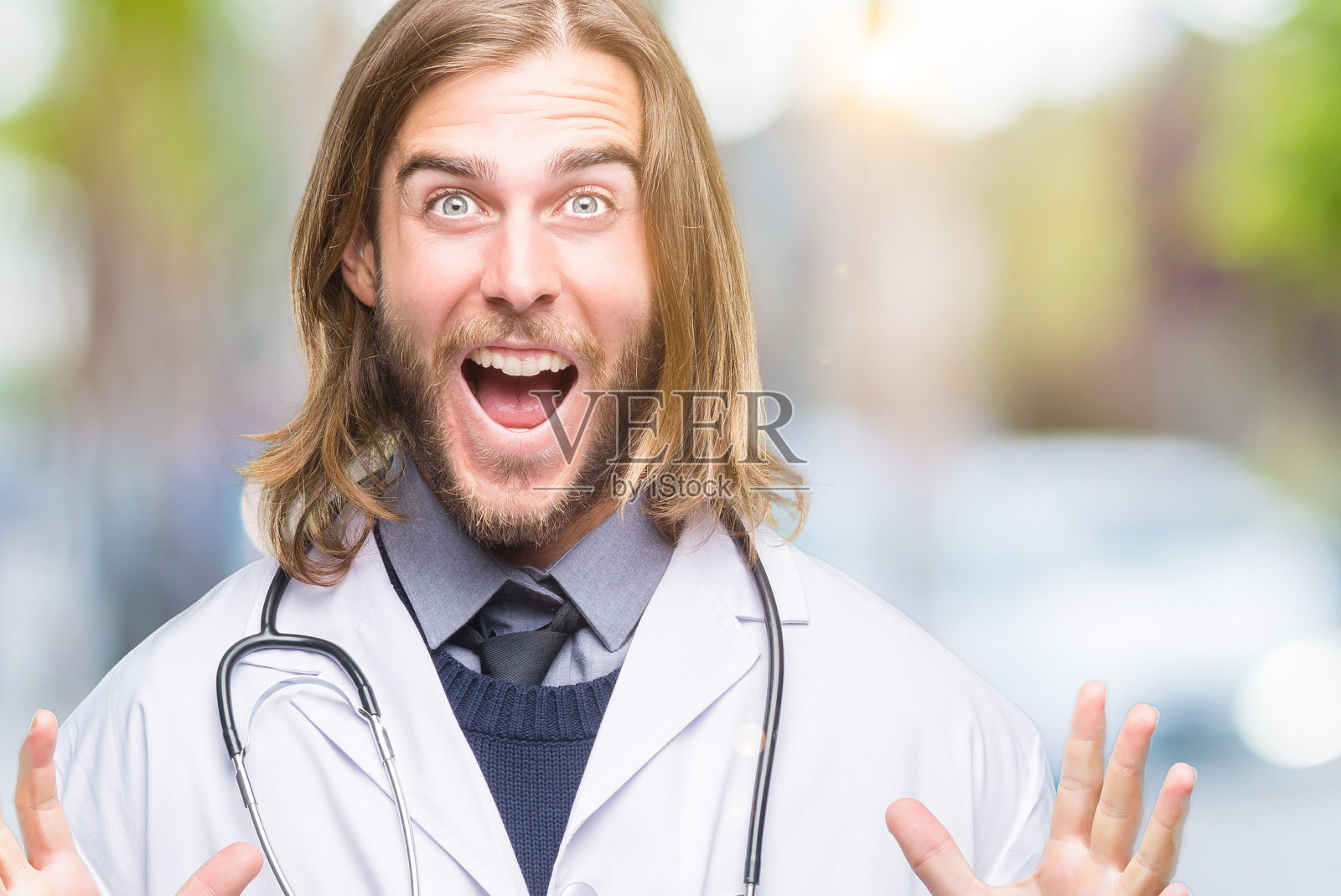 年轻英俊的医生男人长头发在孤立的背景庆祝疯狂和对成功的惊讶，举起手臂，睁开眼睛兴奋地尖叫。赢家的概念照片摄影图片