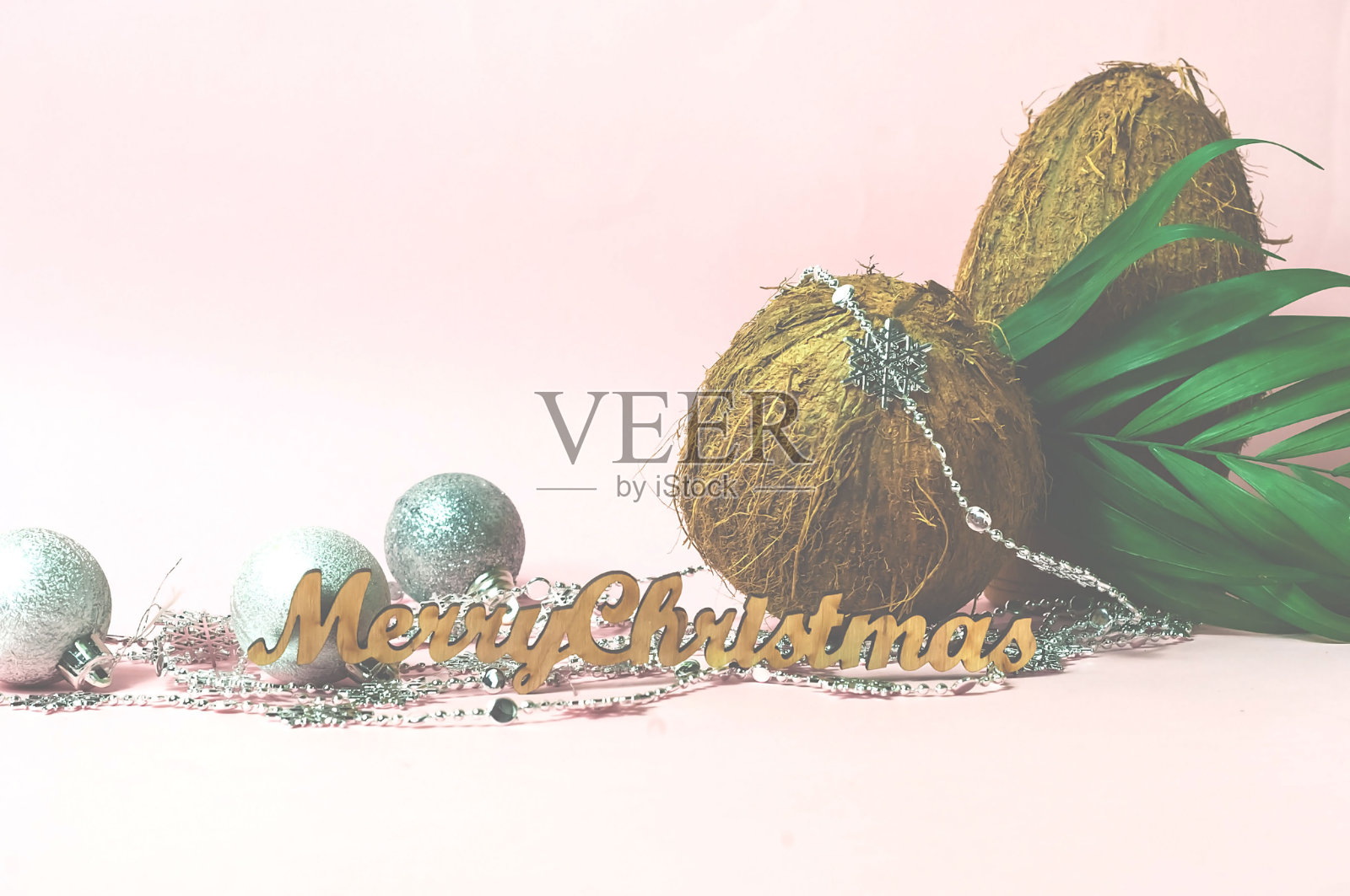 椰子油和热带椰子的创意布局，新年假期的概念。装饰花环和银球在粉红色的背景。照片摄影图片
