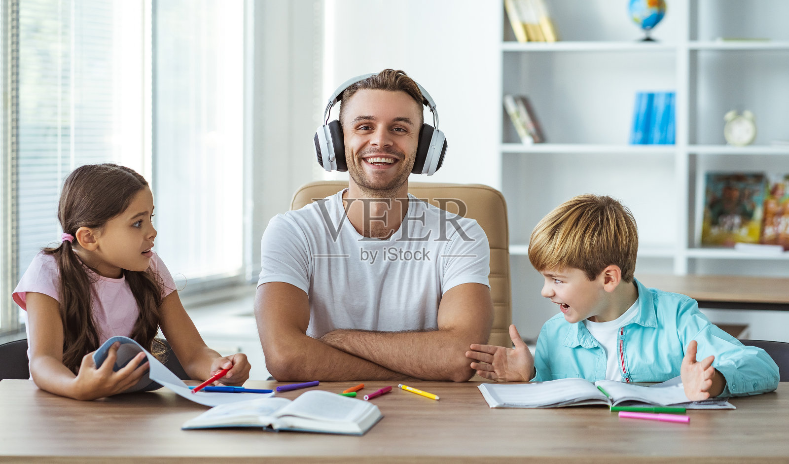 戴着耳机和孩子们坐在桌前的快乐父亲照片摄影图片