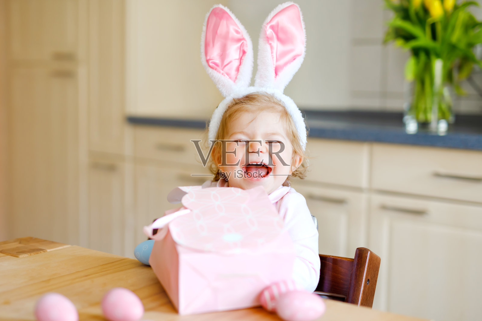 可爱的小女孩戴着复活节兔子耳朵玩彩色彩蛋。快乐宝宝拆礼物。可爱的健康微笑的孩子在粉红色的衣服享受家庭假日照片摄影图片