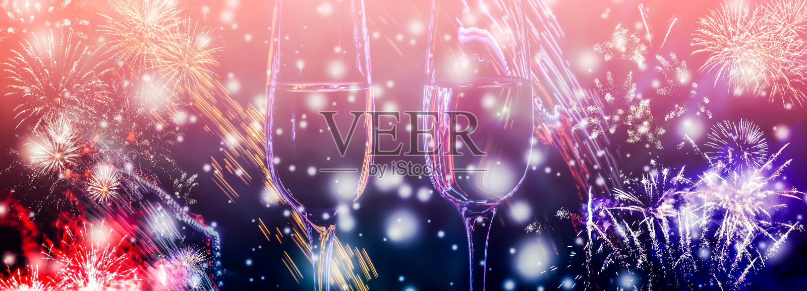 彩色的烟花和两杯起泡的香槟酒与泡沫近距离在飘落的雪背景。照片摄影图片