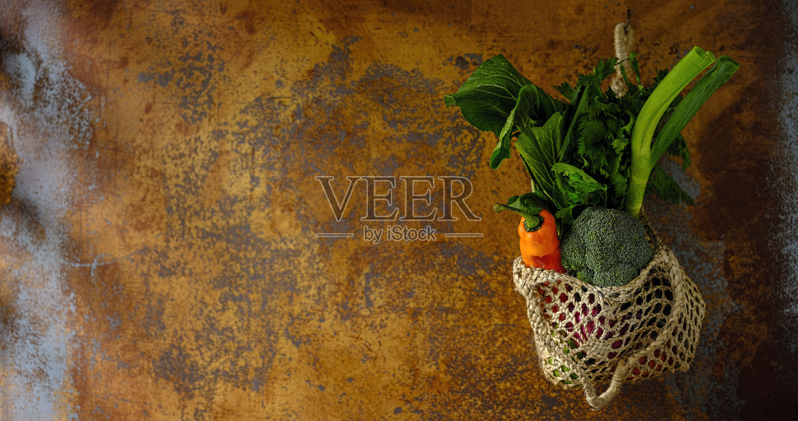 许多色彩鲜明的沙拉蔬菜在一个可重复使用的绳黄麻袋挂在一个抽象的赤陶土橙色背景墙上。照片摄影图片