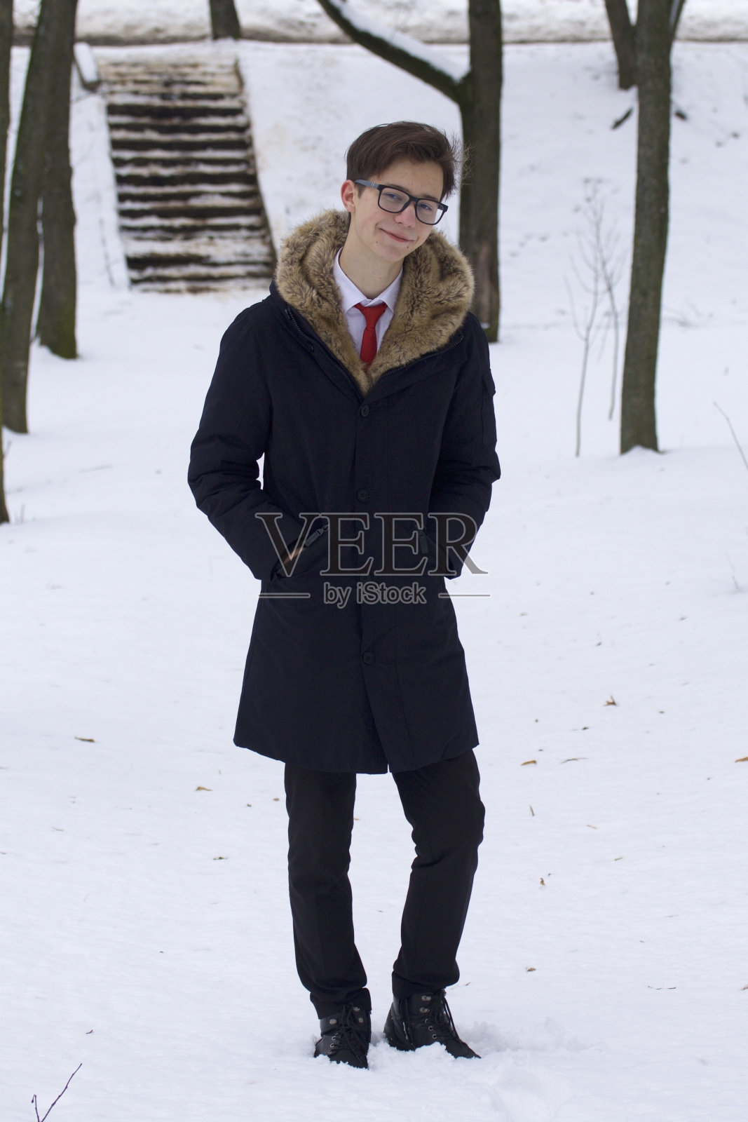 一个年轻人的肖像穿着一件有毛皮领子的外套。在冬天的公园散步。照片摄影图片