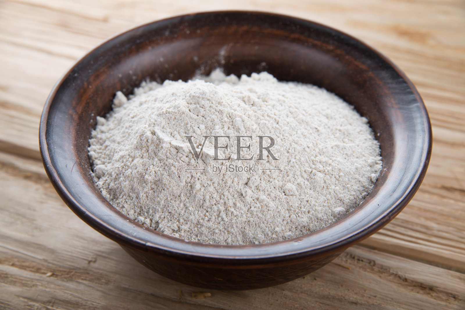 白色的桌子上放着一个盛满面粉的泥盘子。照片摄影图片