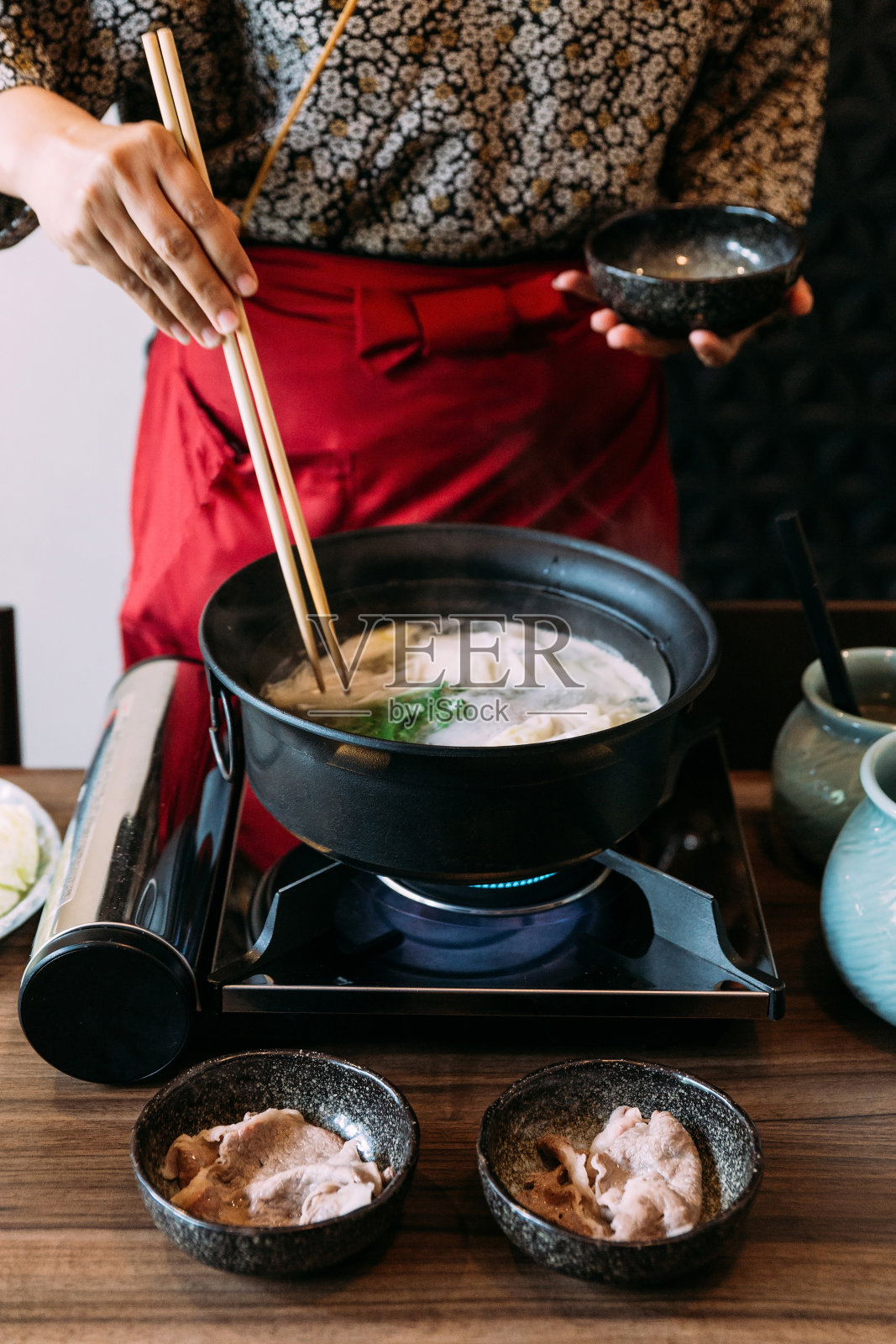 一名身穿和服的妇女正在煮一套Sukiyaki蔬菜，包括卷心菜、假小白菜、胡萝卜、香菇、木槿和豆腐。照片摄影图片