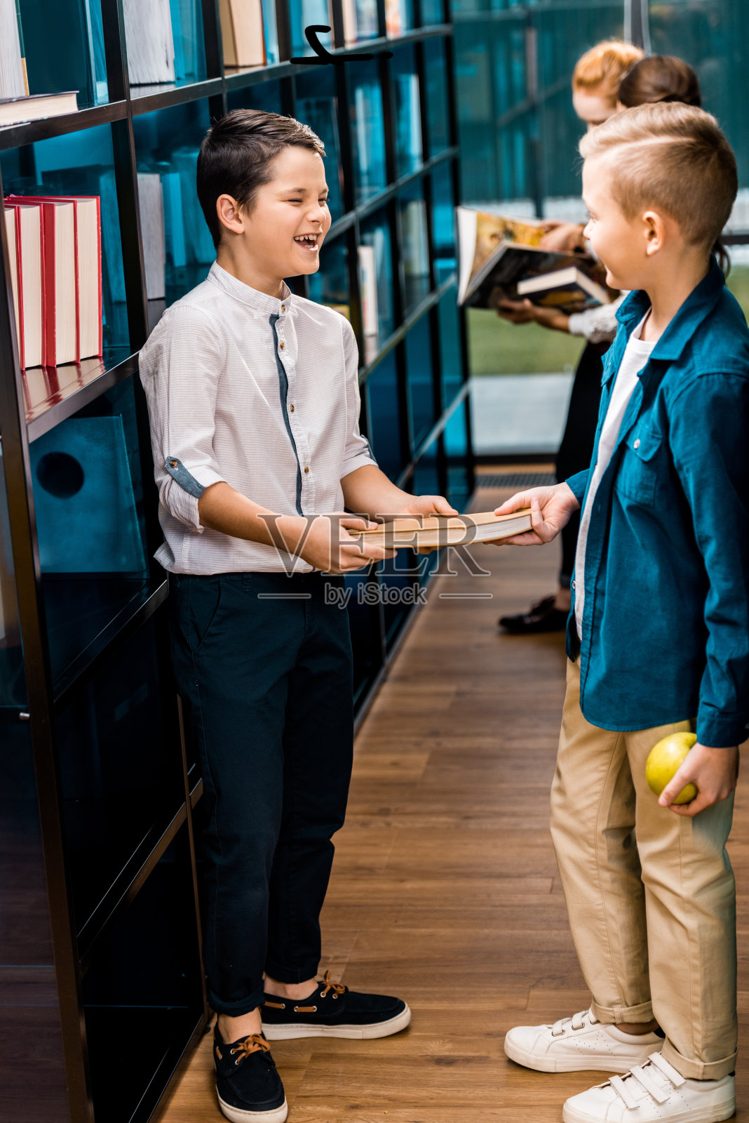 可爱的小学生拿着书，在图书馆里互相微笑照片摄影图片