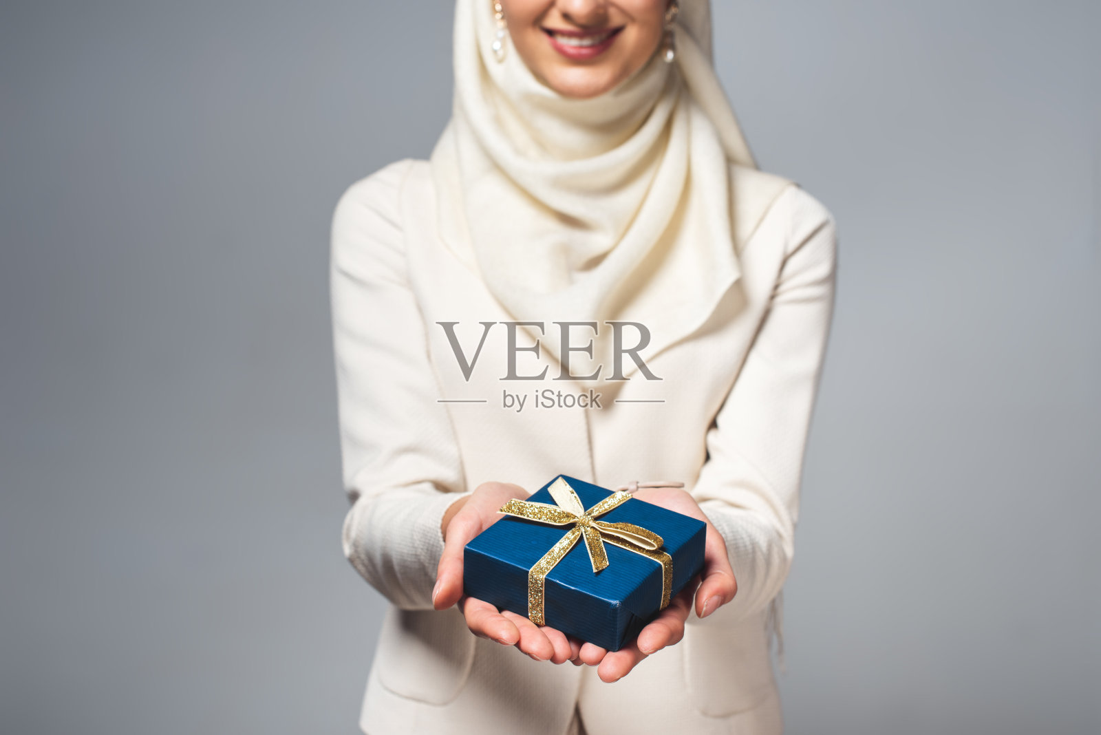 微笑的年轻穆斯林妇女抱着礼物盒孤立在灰色的镜头照片摄影图片