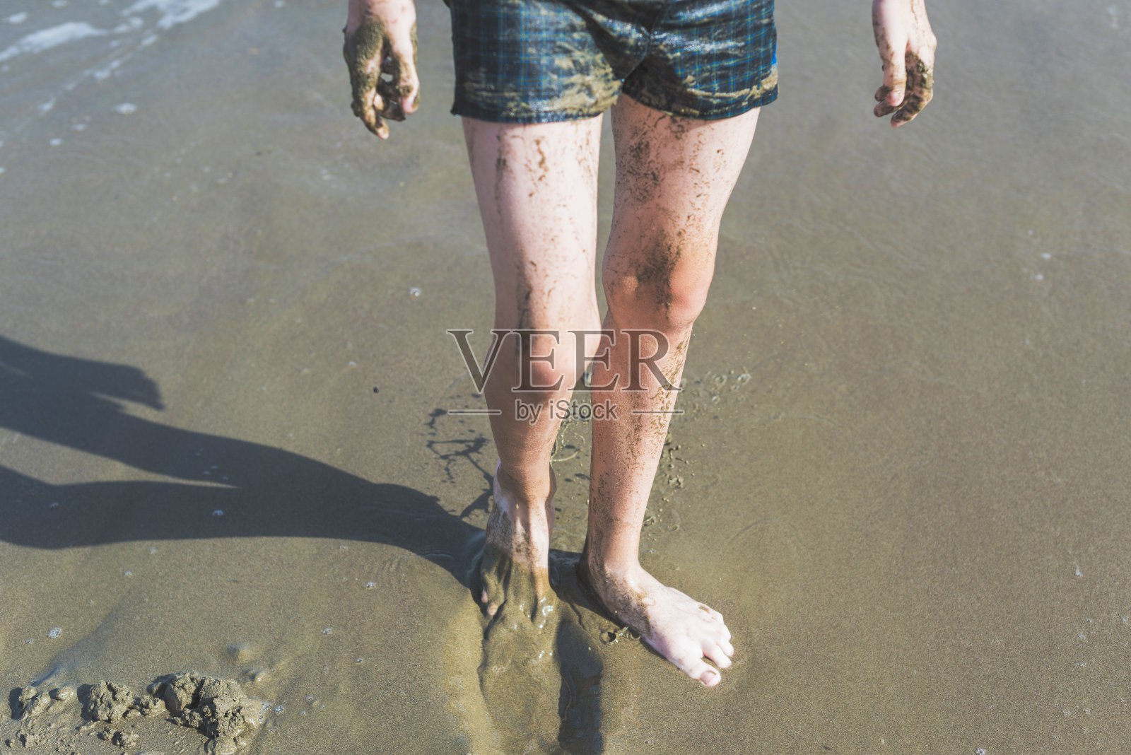 在海滩上，快乐的少年的腿在愈合的泥从海中照片摄影图片