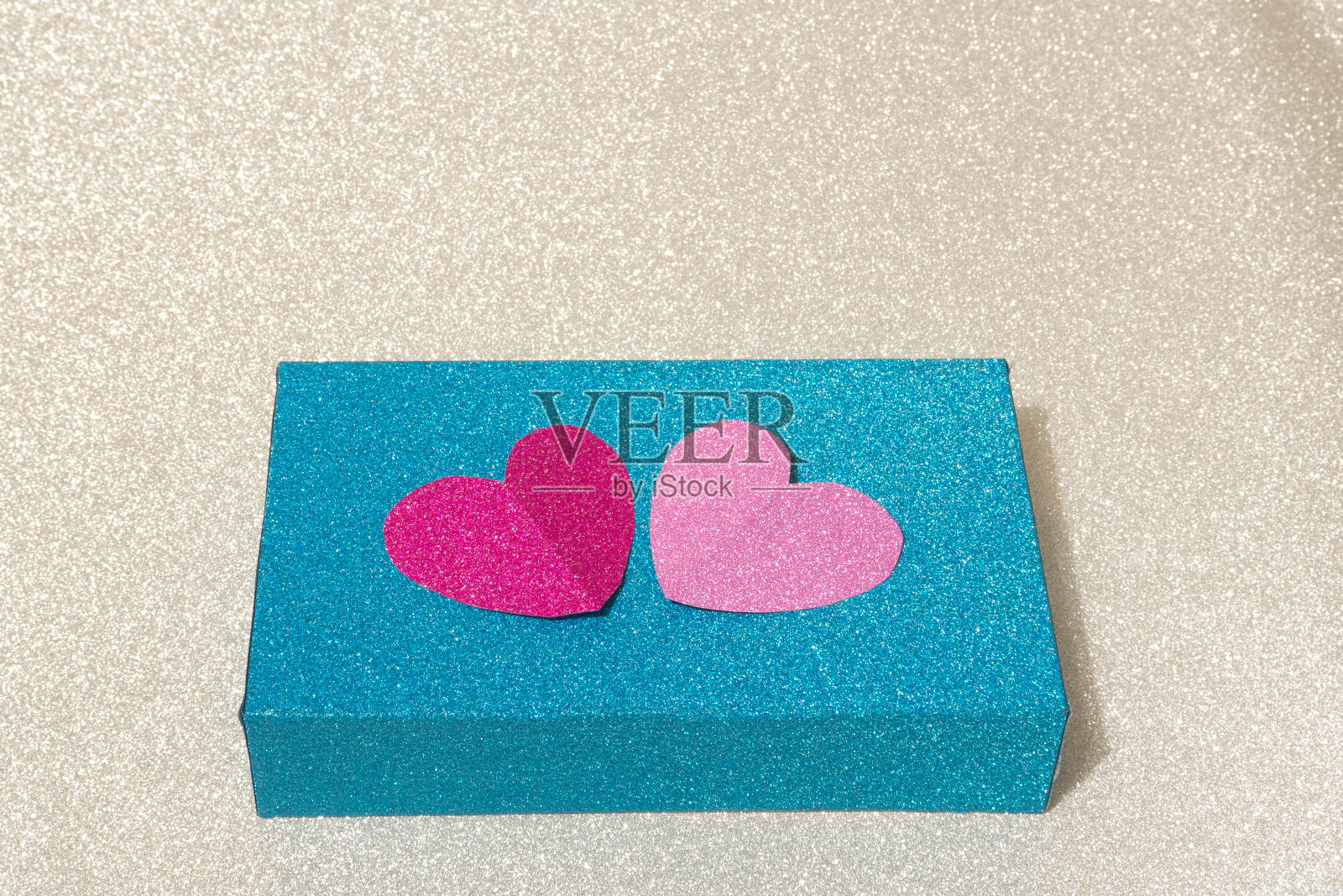 一个蓝色的盒子，银色的背景上装饰着粉色和红色的心。概念上的照片摄影图片