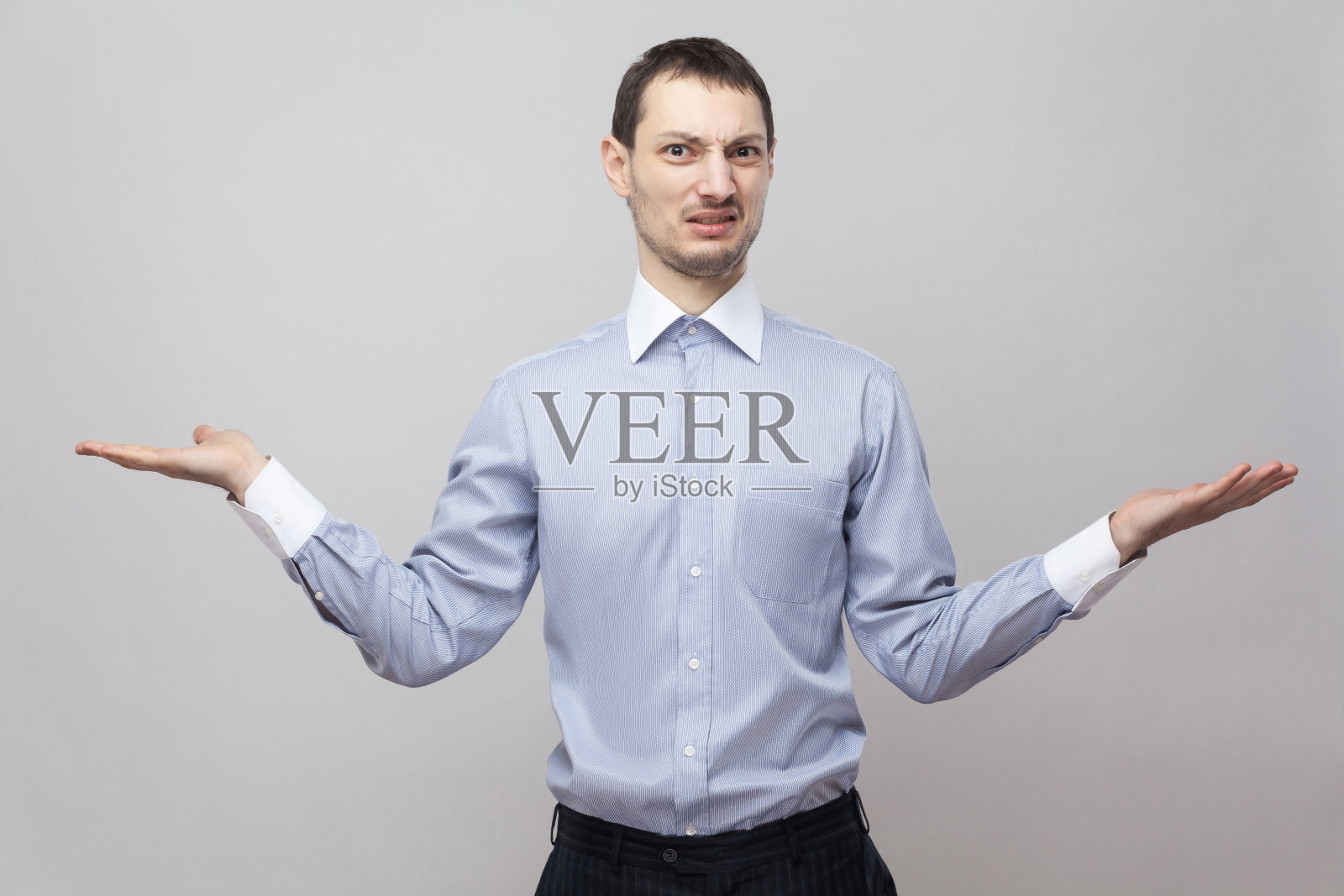 我不知道该选哪一个。一幅困惑的商人肖像，穿着蓝色衬衫，举着胳膊看着镜头。照片摄影图片