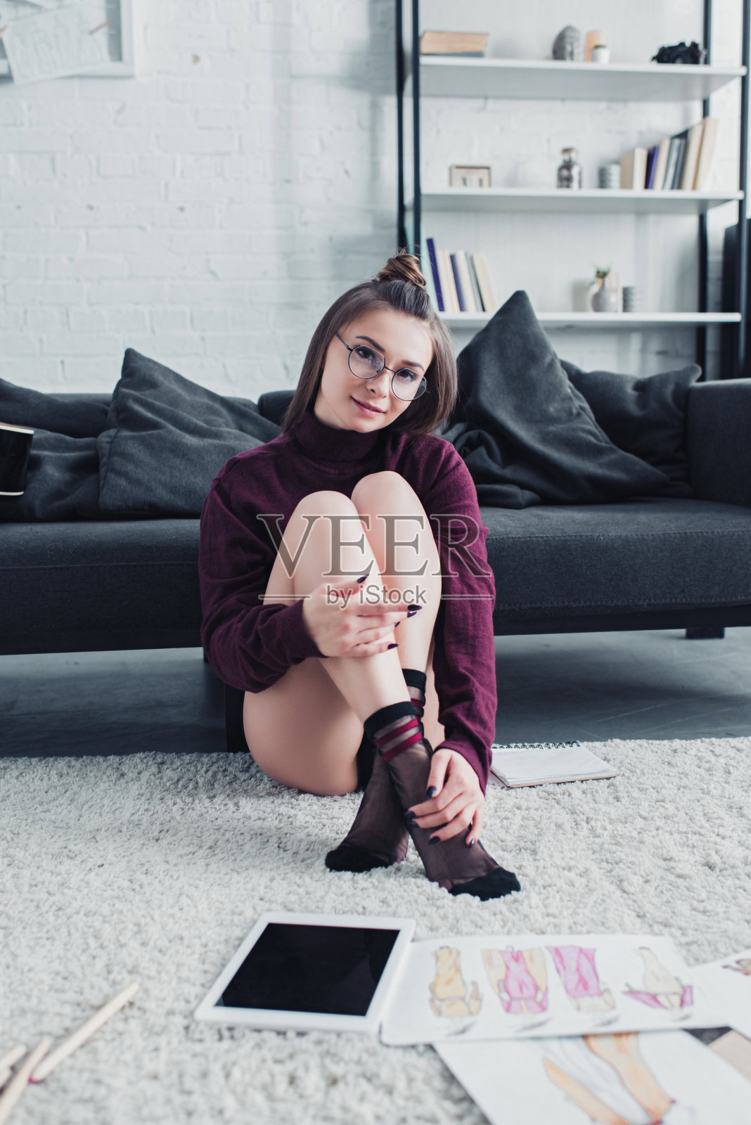 迷人的设计师坐在沙发旁边的地毯上，看着客厅里的相机照片摄影图片