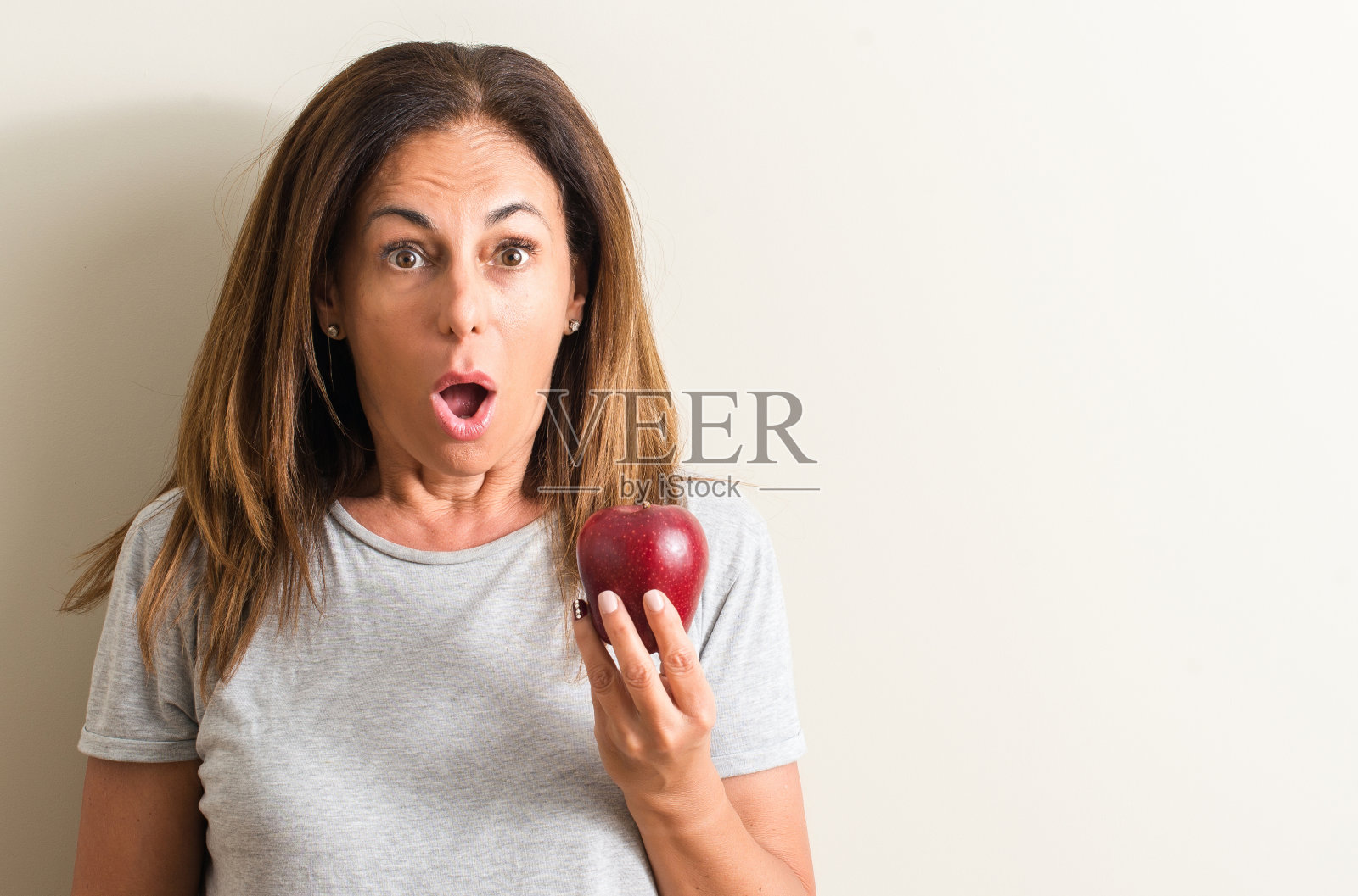 中年妇女捧着一个青涩的苹果吓得脸上带着惊讶、害怕和兴奋的恐惧表情照片摄影图片