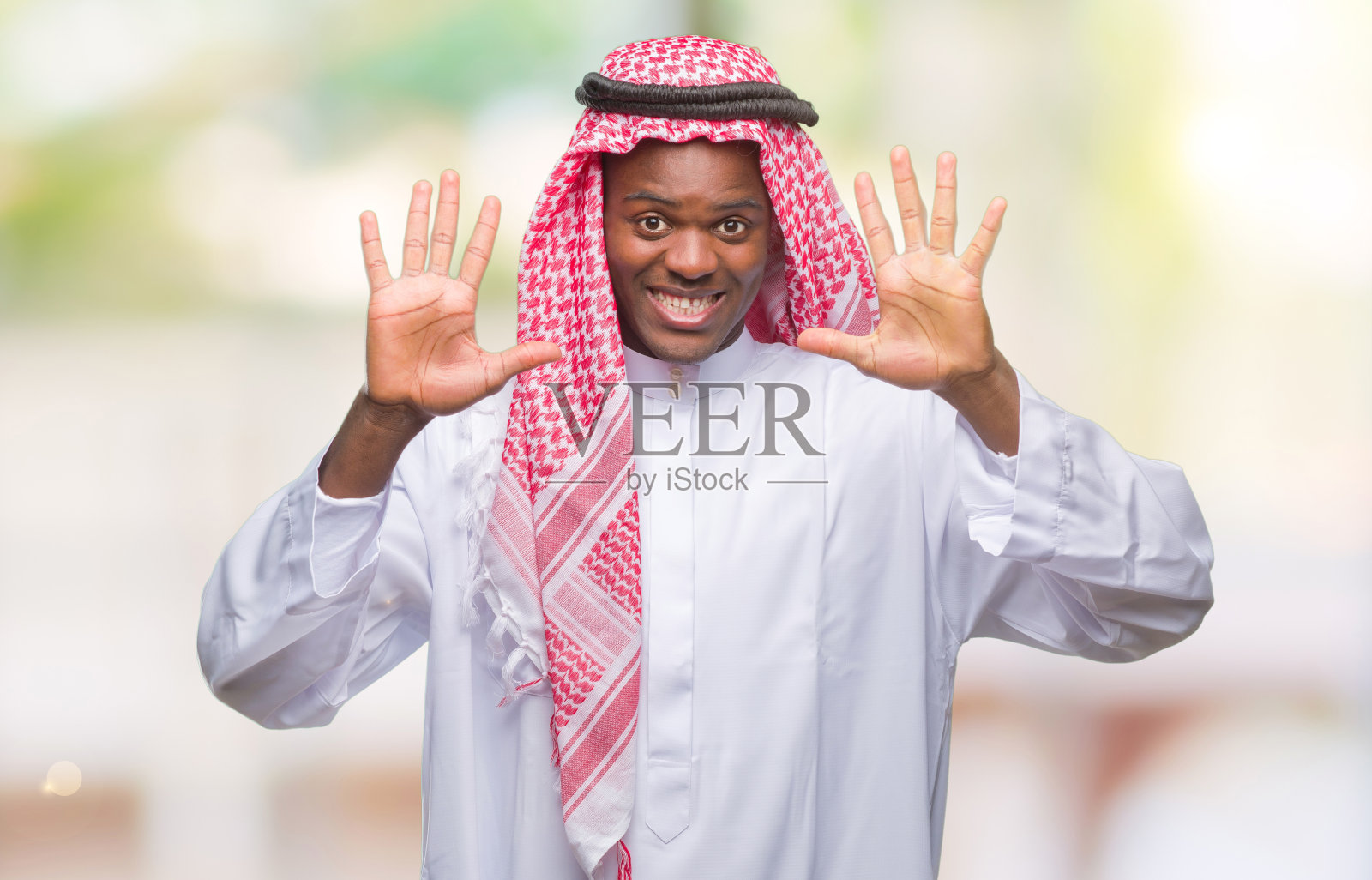 年轻的阿拉伯裔非洲男子穿着传统的keffiyeh在孤立的背景显示和指向十号手指，同时自信和快乐的微笑。照片摄影图片