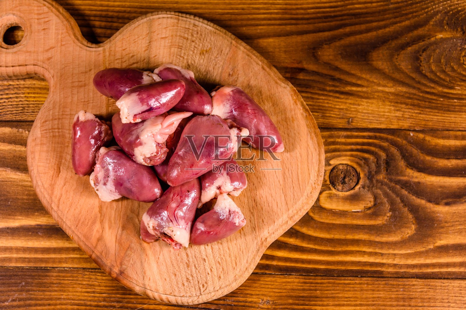 木桌上的切菜板上有生鸡心。俯视图照片摄影图片