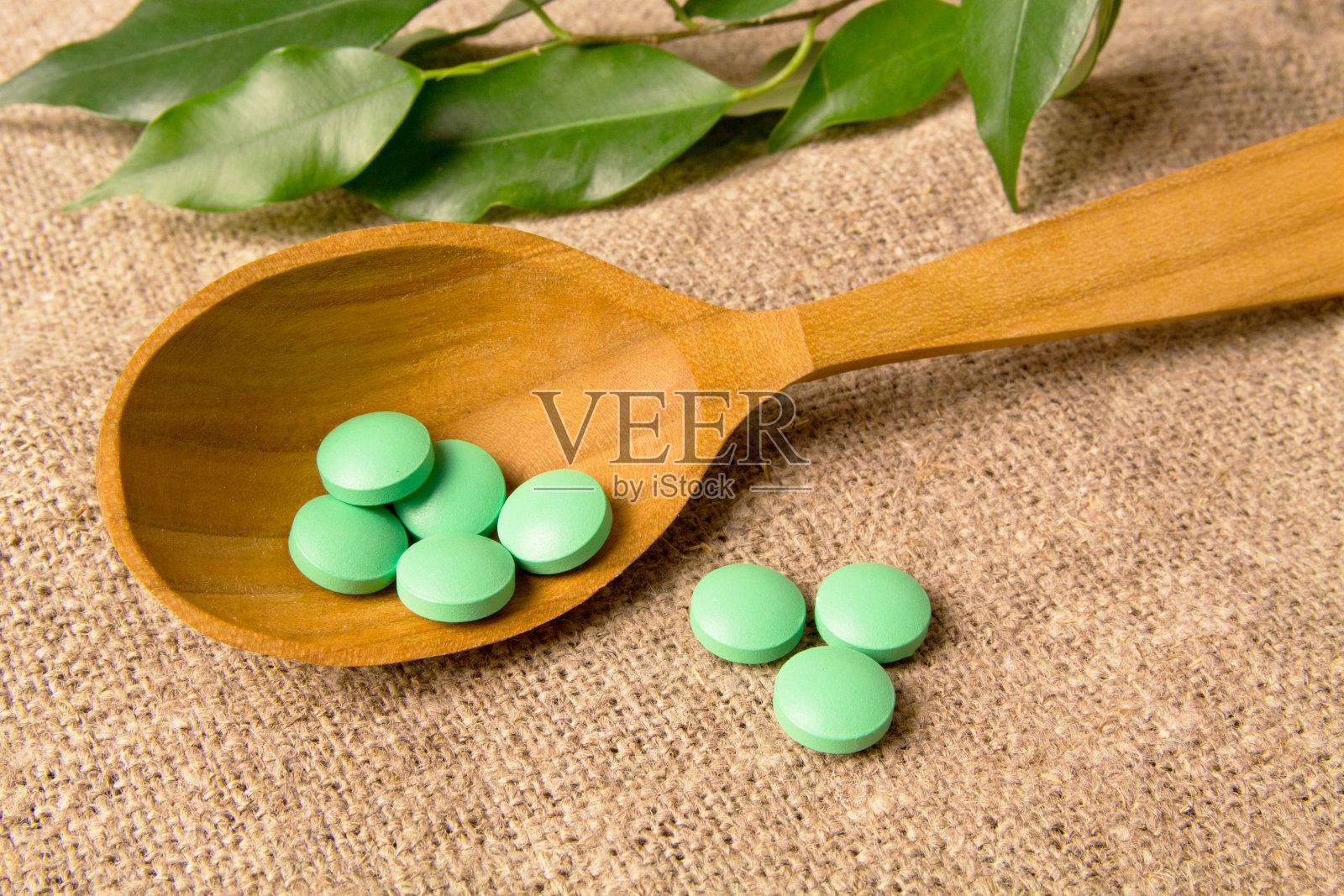 中草药药丸在木勺上的药用叶子背景上。草药制药丸照片摄影图片