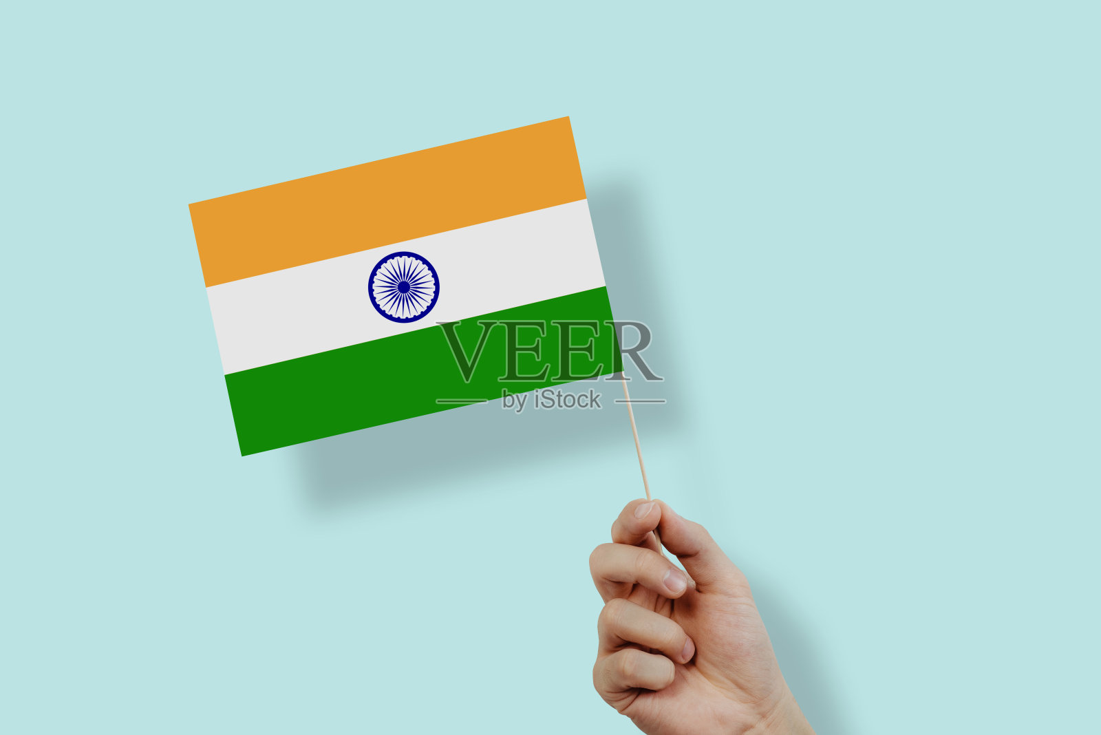 一只手举着淡蓝色背景上的印度国旗。照片摄影图片
