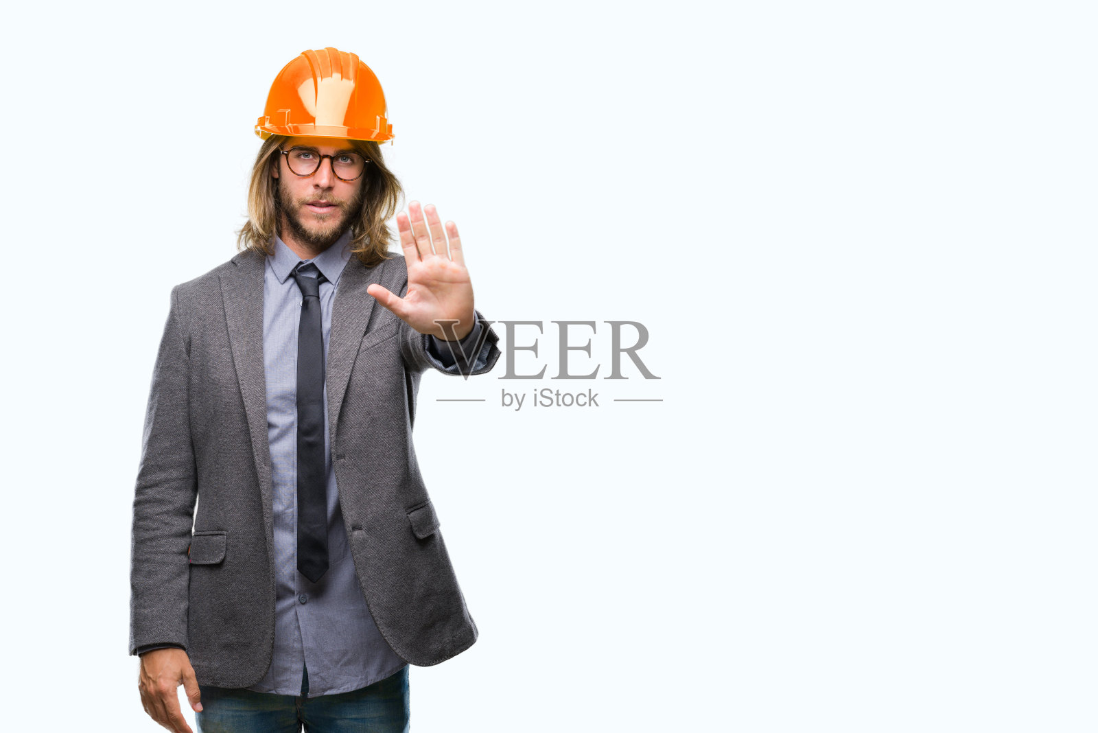 年轻英俊的建筑师长头发戴着安全帽在孤立的背景上做着停止用手掌唱歌。警告表情与否定和严肃的手势在脸上。照片摄影图片