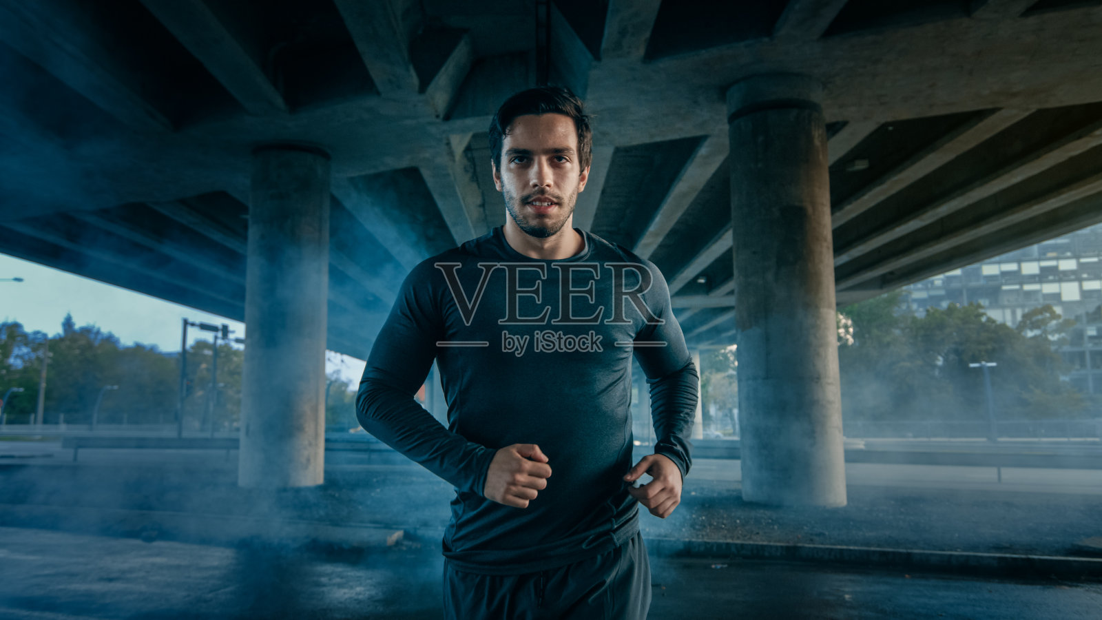 肖像拍摄的一个运动员肌肉的年轻人在运动服装慢跑在街上。他在桥下的城市环境中跑步。照片摄影图片