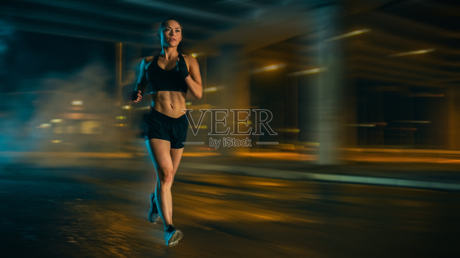 一个美丽的健身女孩穿着黑色运动上衣和短裤在街上慢跑。她正在一个夜晚潮湿的城市环境中锻炼。通过工作时间。照片摄影图片