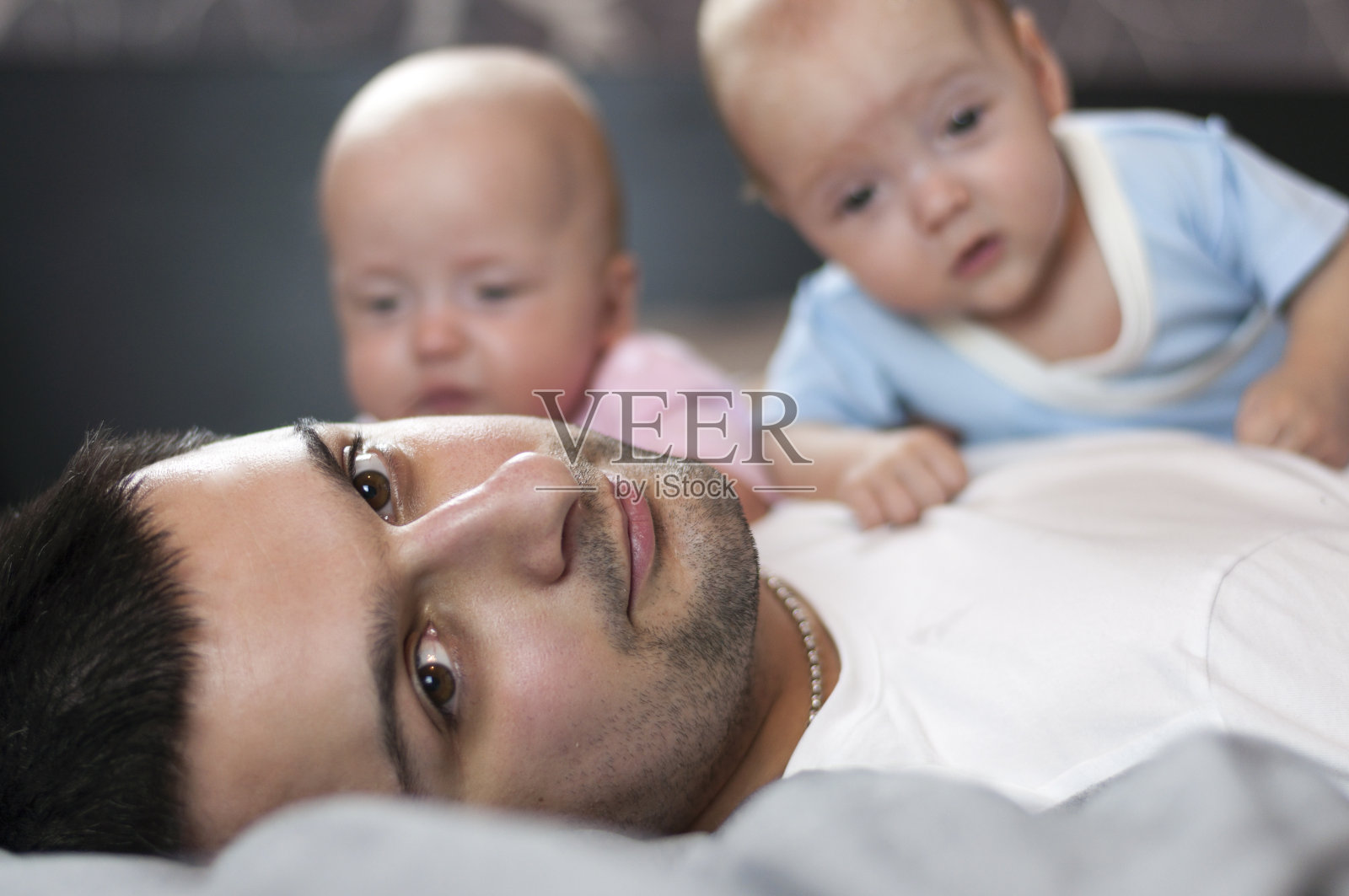 年轻的父亲和刚出生的双胞胎躺在床上。有选择性的重点。照片摄影图片