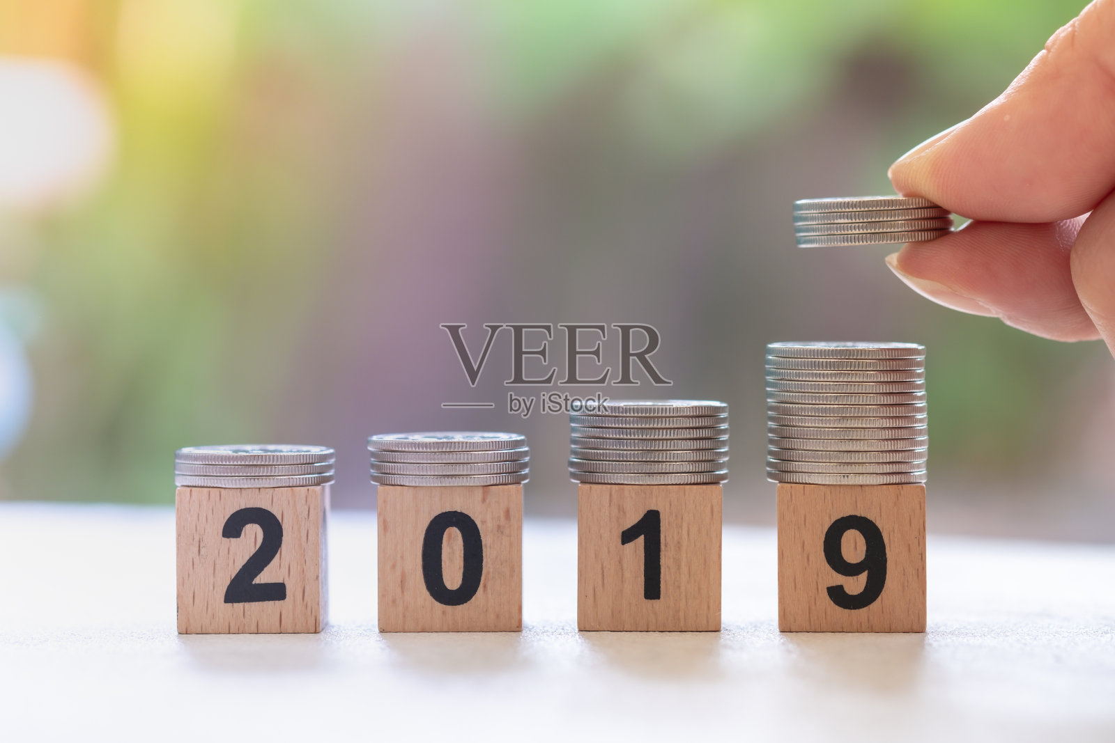 2019年新年，节约理念。紧叠的银币在数字木块上与人的手，并把一叠硬币在堆栈的顶部照片摄影图片
