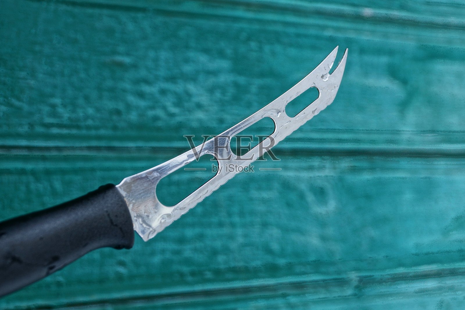 在绿色墙壁的背景下，有黑色把手的奶酪刀照片摄影图片