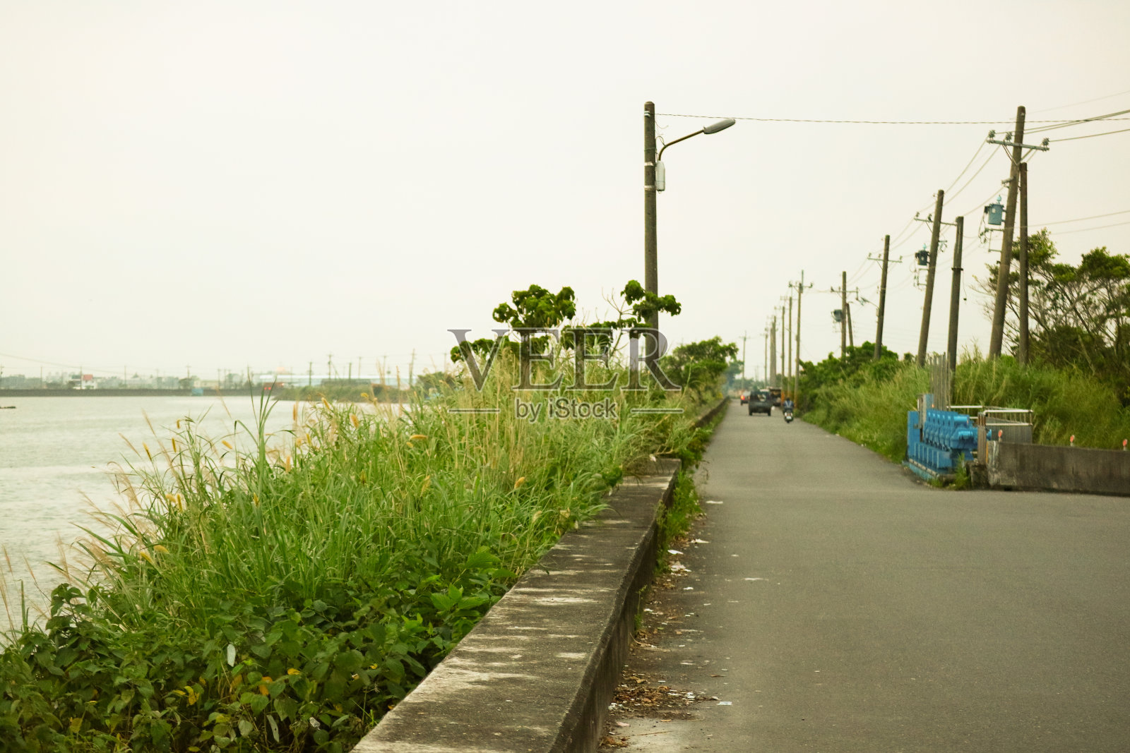 在一片郁郁葱葱的草地旁，是安静的、波浪形的河流，还有直通到前面的笔直的乡村道路。照片摄影图片