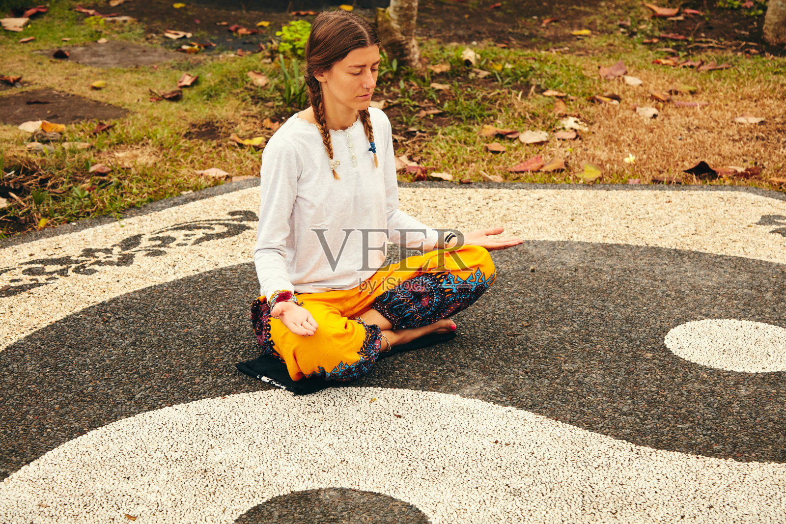 年轻女子练习瑜伽-冥想在热带花园与阴阳标志。照片摄影图片