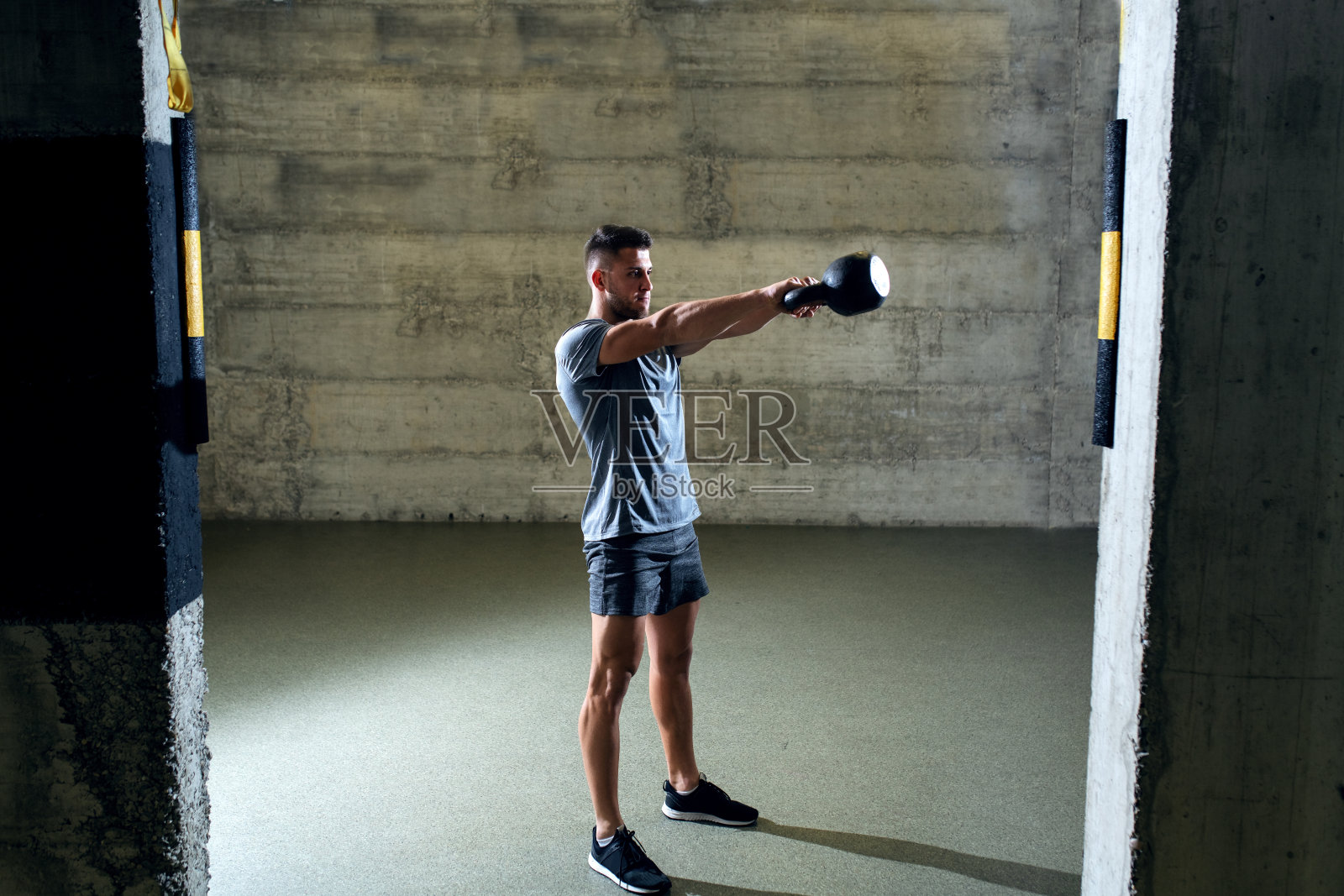 专注的肌肉男人在运动服装做练习壶铃，而站在体育馆。照片摄影图片