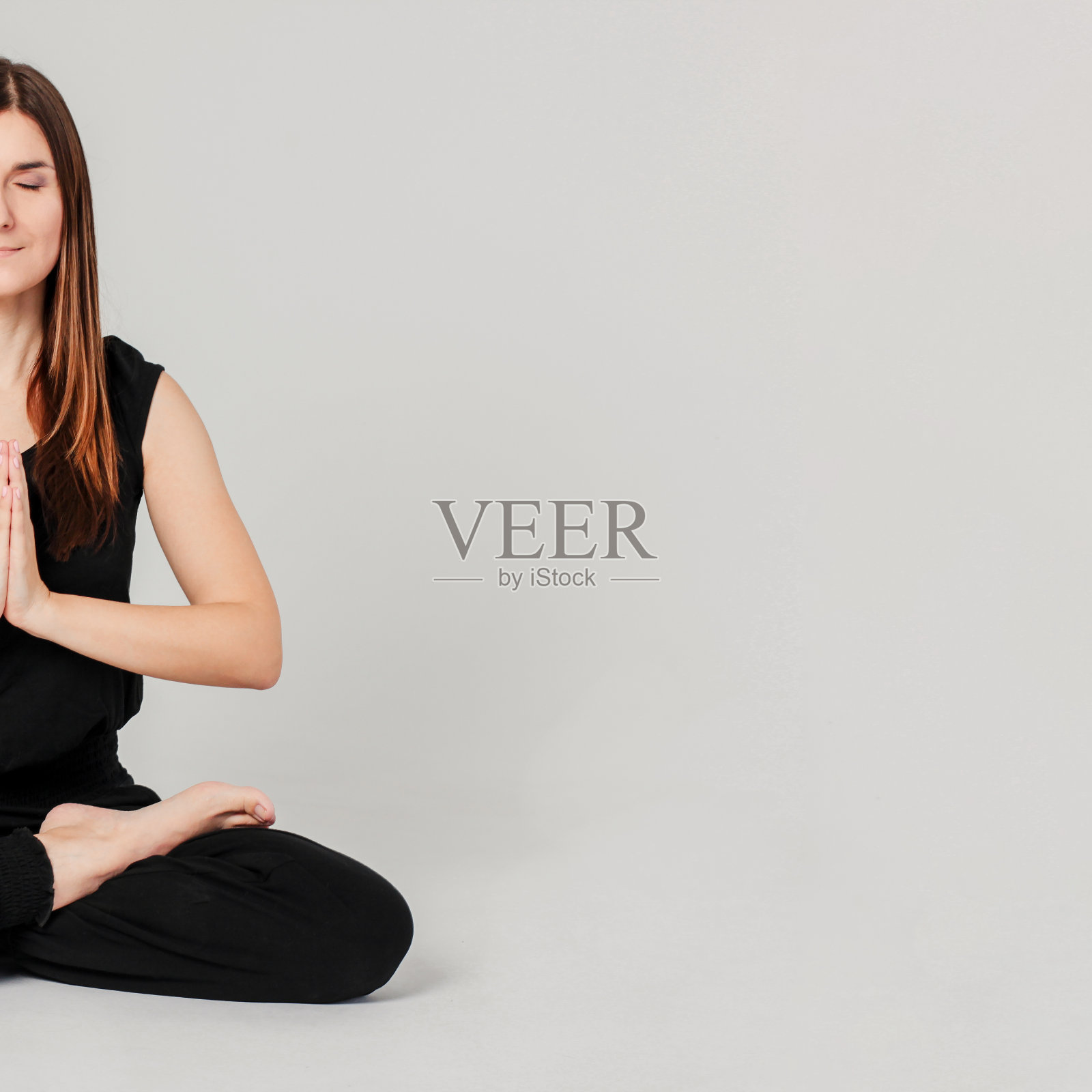 年轻的黑发苗条的女人在黑色坐在莲花位置瑜伽孤立在灰色的背景照片摄影图片